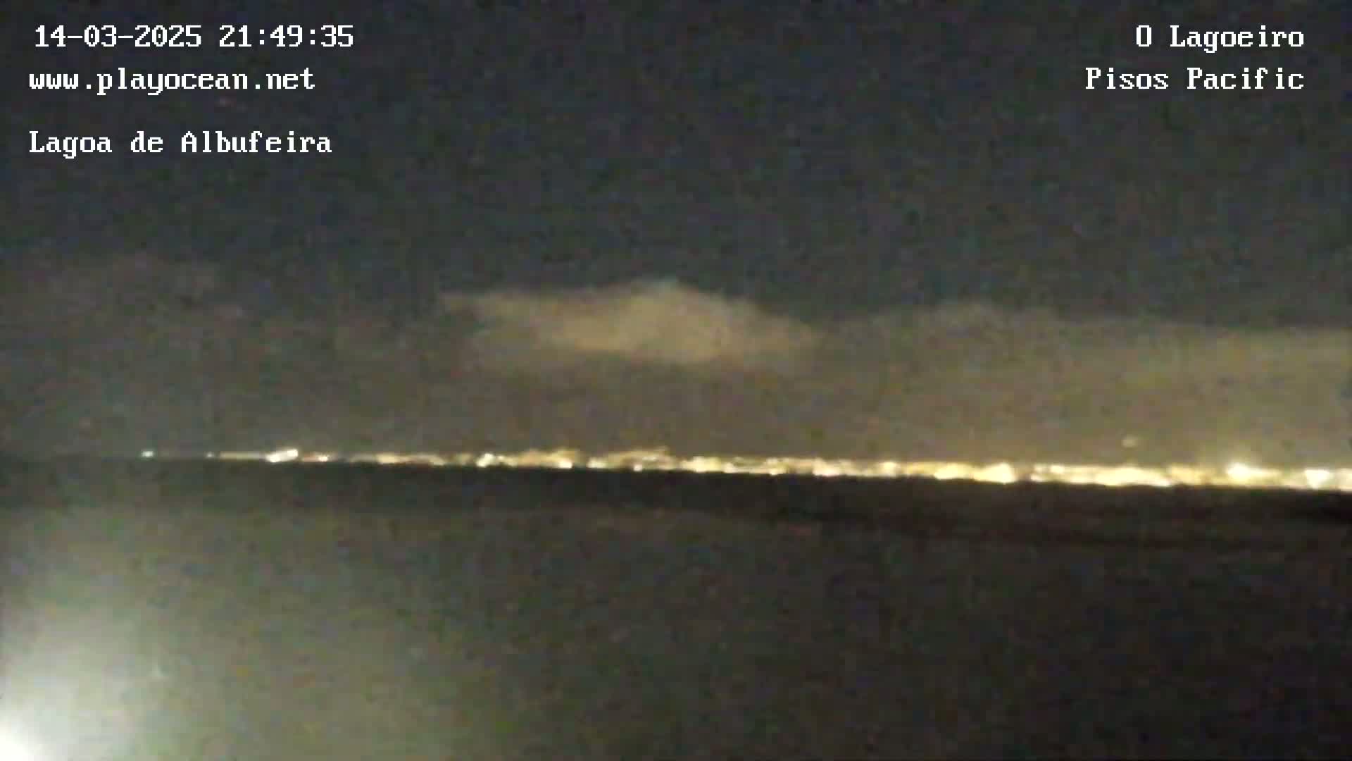 A nighttime view shows a distant city skyline illuminated under a partly cloudy sky.