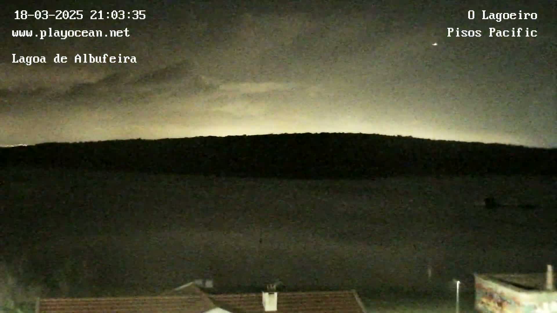 A nighttime view shows a dark, silhouetted hill against a cloudy, light-grey sky.