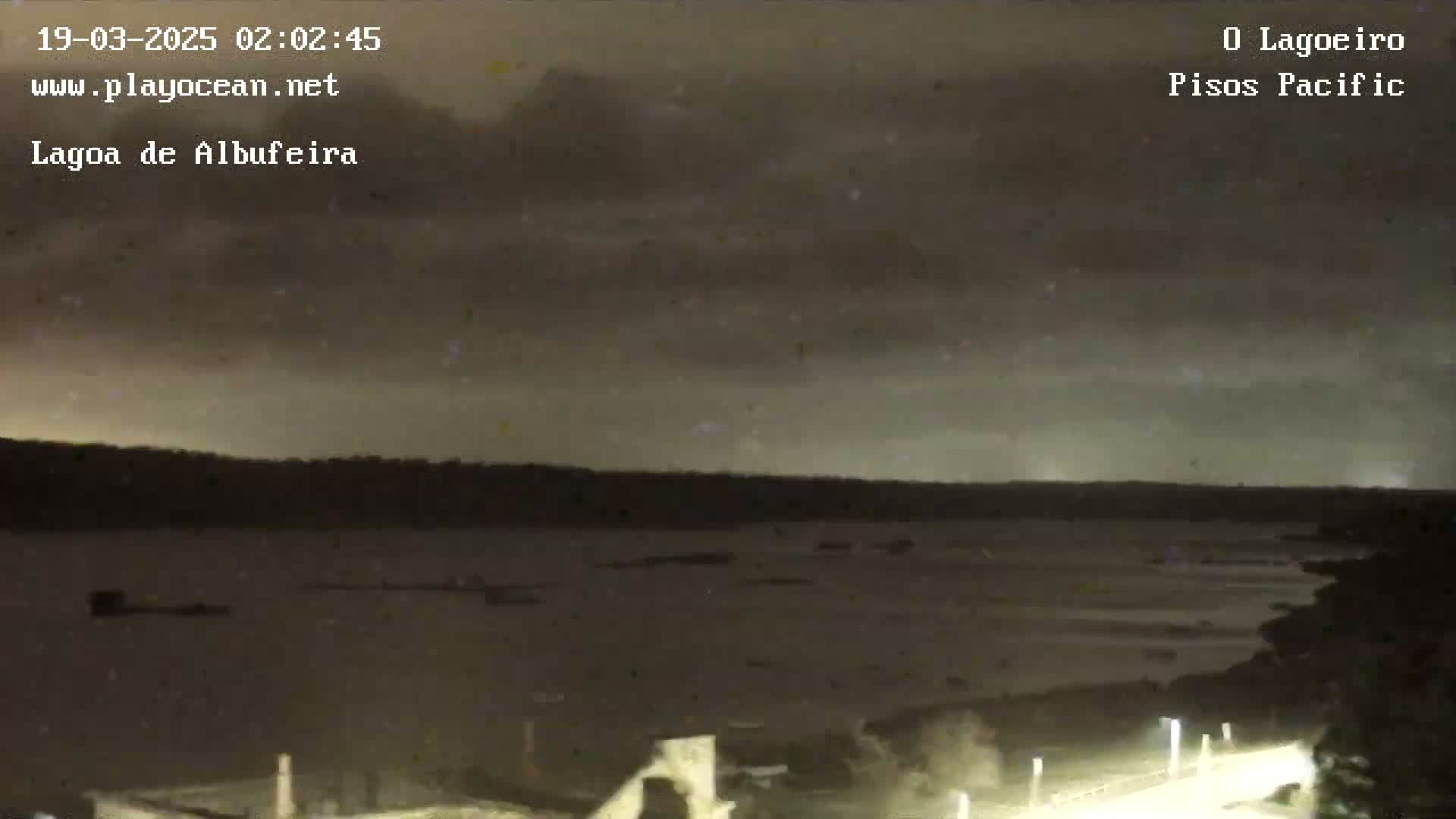 A nighttime view of a dark body of water under a cloudy sky, with a bridge and lights visible in the foreground.