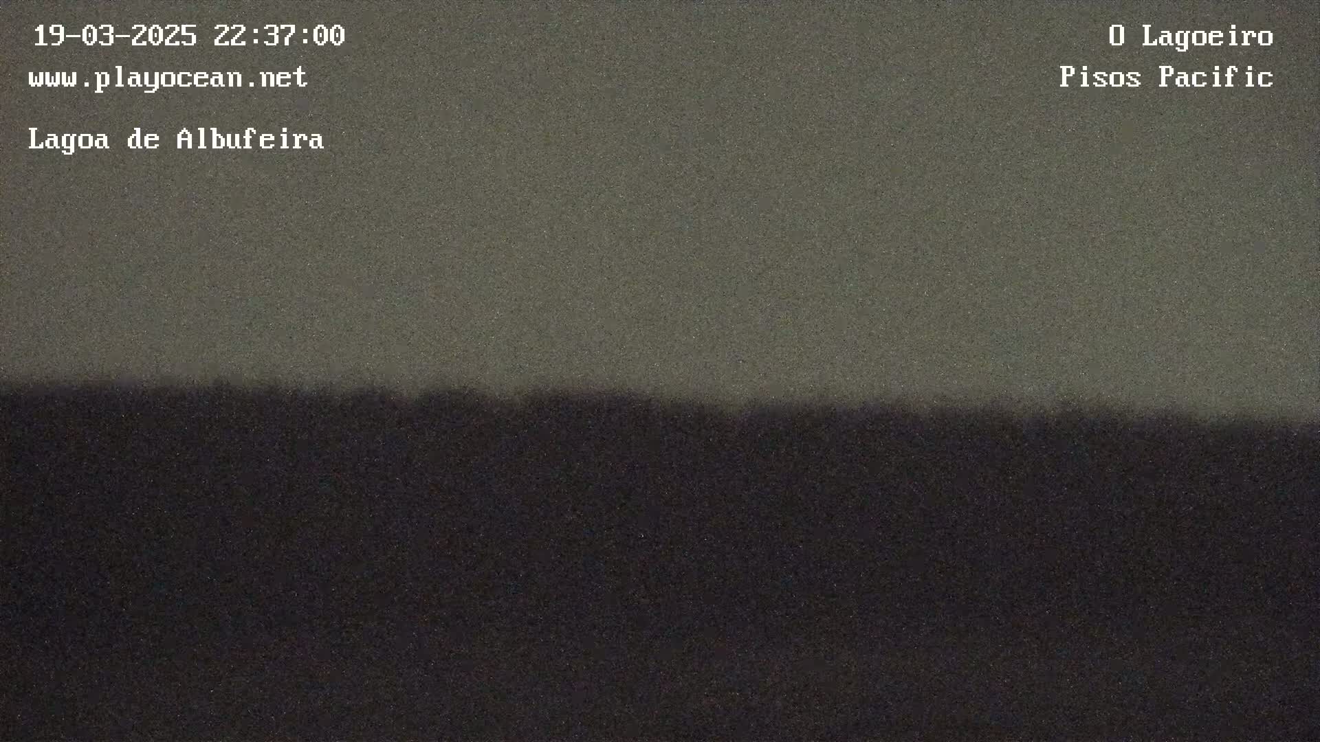 A dark, low-light image shows a dark horizon line separating a slightly lighter, muted gray sky from a completely dark landmass.