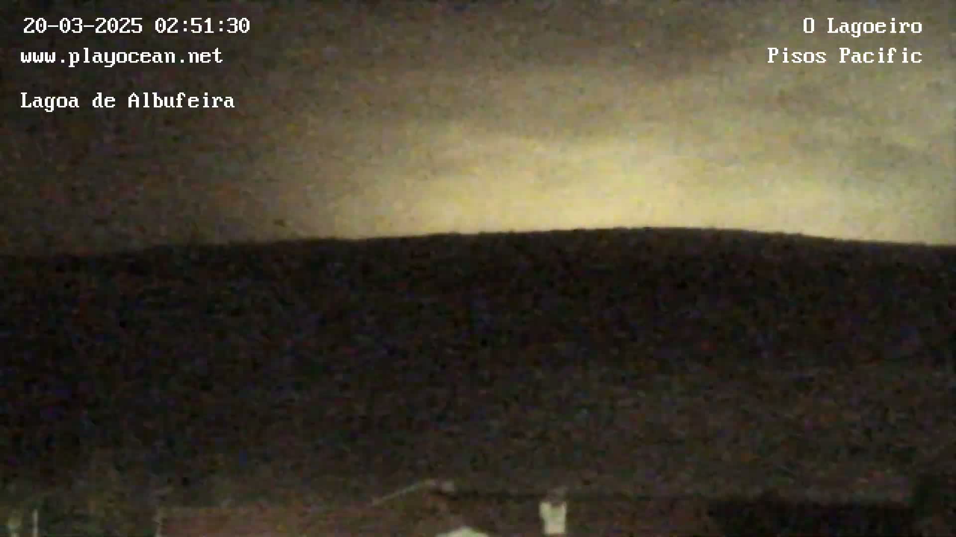 A dark, low-light outdoor scene shows a land horizon under a pale, yellowish-white sky at night.