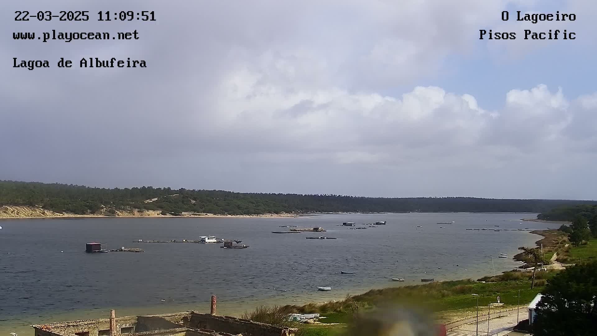 A calm body of water dotted with small structures and boats under a partly cloudy sky.
