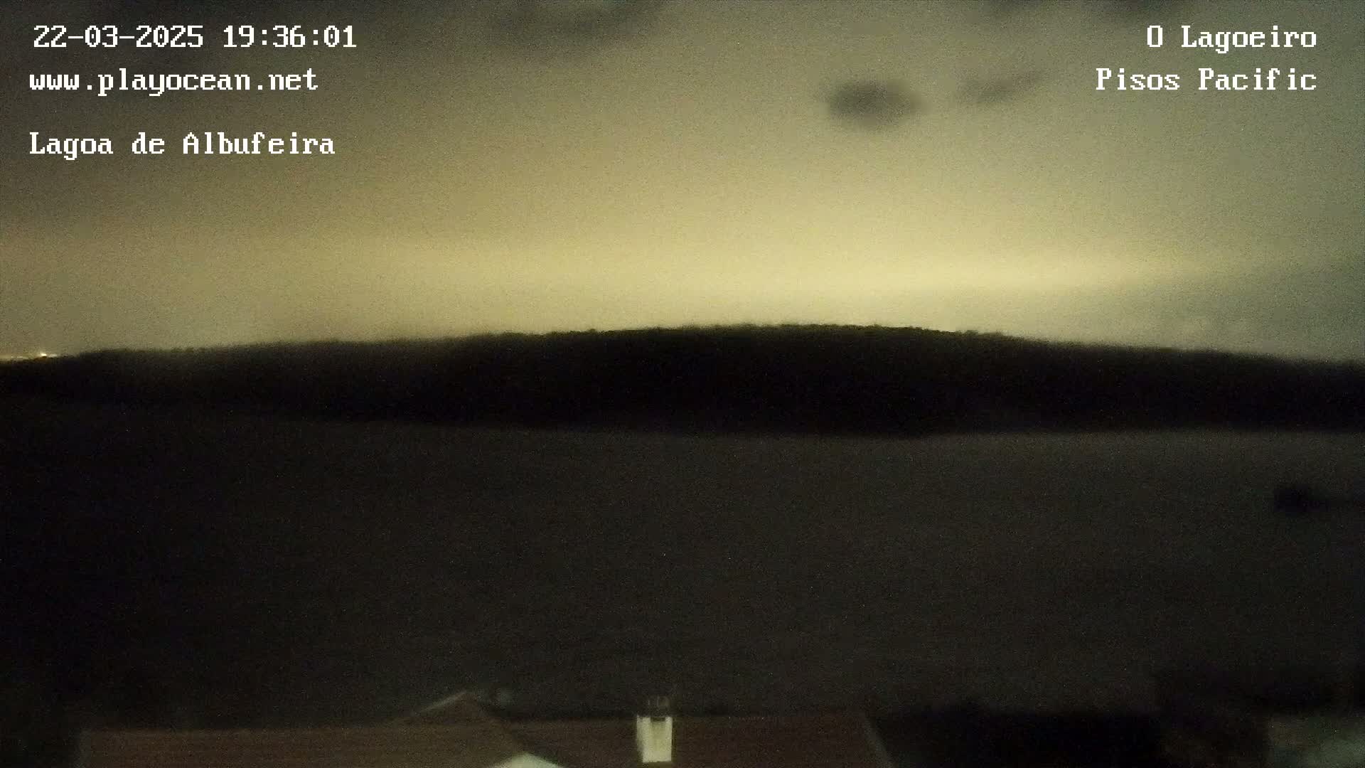 A dark, silhouetted landmass is visible across a body of still water under a dusky, possibly nighttime sky.