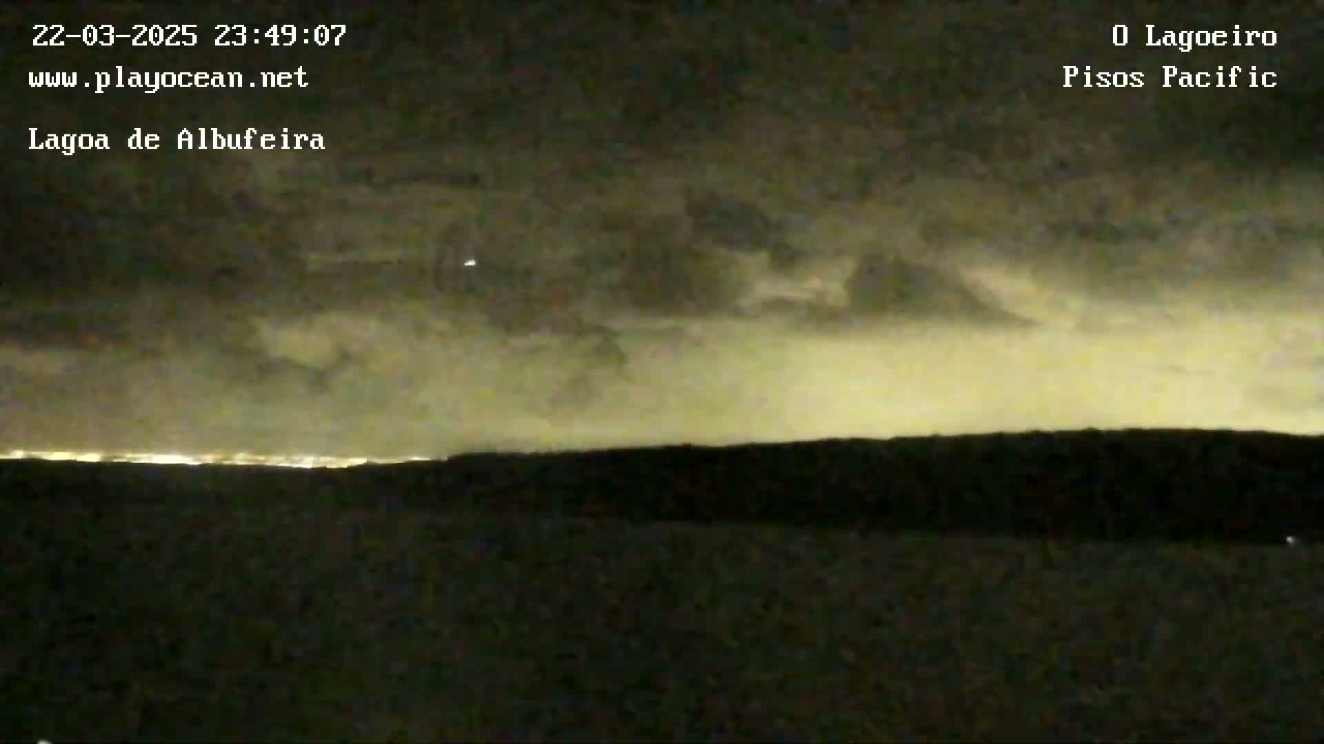 A nighttime, cloudy view shows a distant city skyline illuminated against a dark, overcast sky.