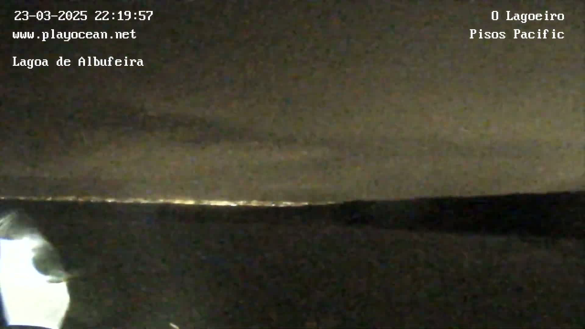 A nighttime view shows a distant line of lights on the horizon under a dark, cloudy sky.