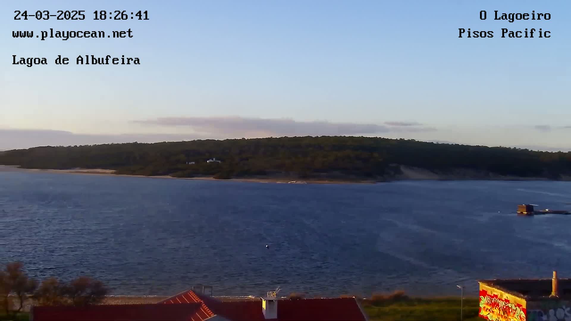 A calm body of water under a clear, twilight sky stretches towards a wooded shoreline.