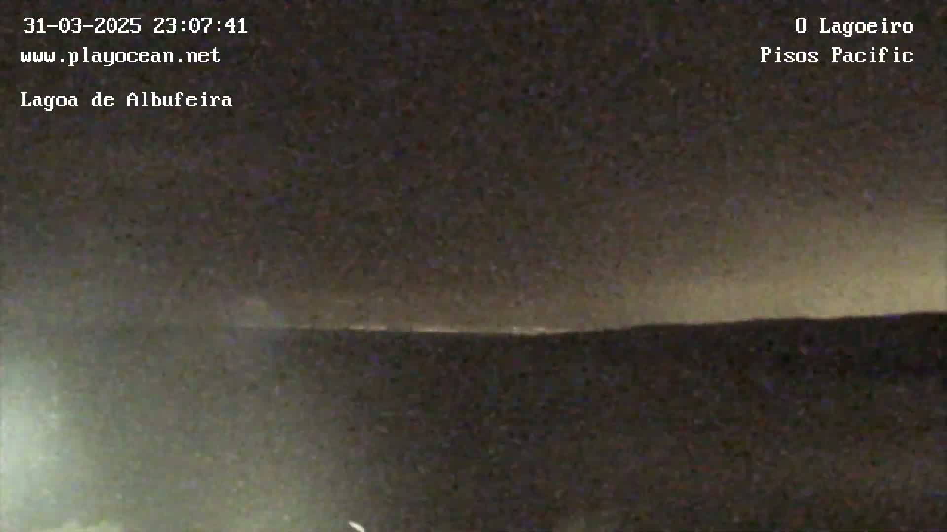 A dark, nighttime landscape is visible, with a faintly illuminated horizon line under a mostly clear sky.