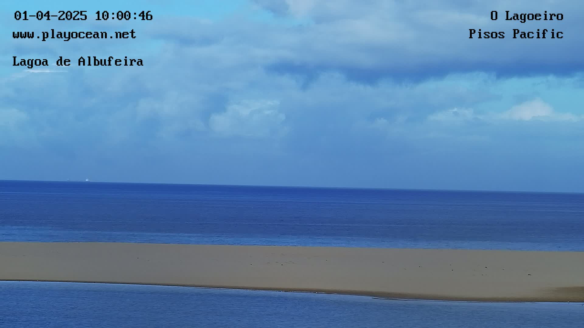 A partly cloudy sky overlooks a calm ocean with a sandy beach visible in the foreground.