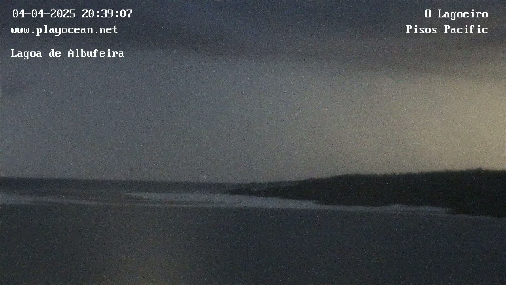 A dark, overcast sky hangs over a calm body of water meeting a dark shoreline at dusk.
