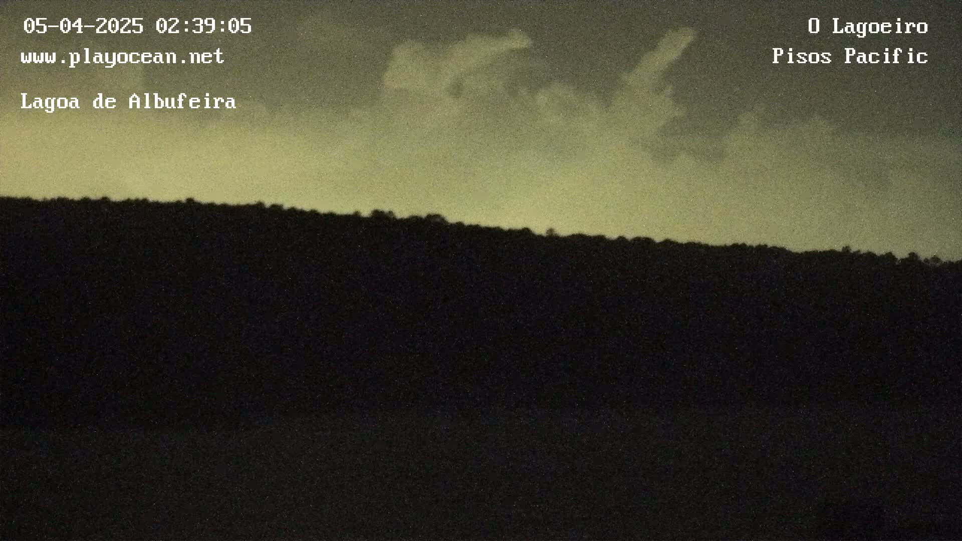 A dark silhouette of a hill is visible against a pale, cloudy evening sky.