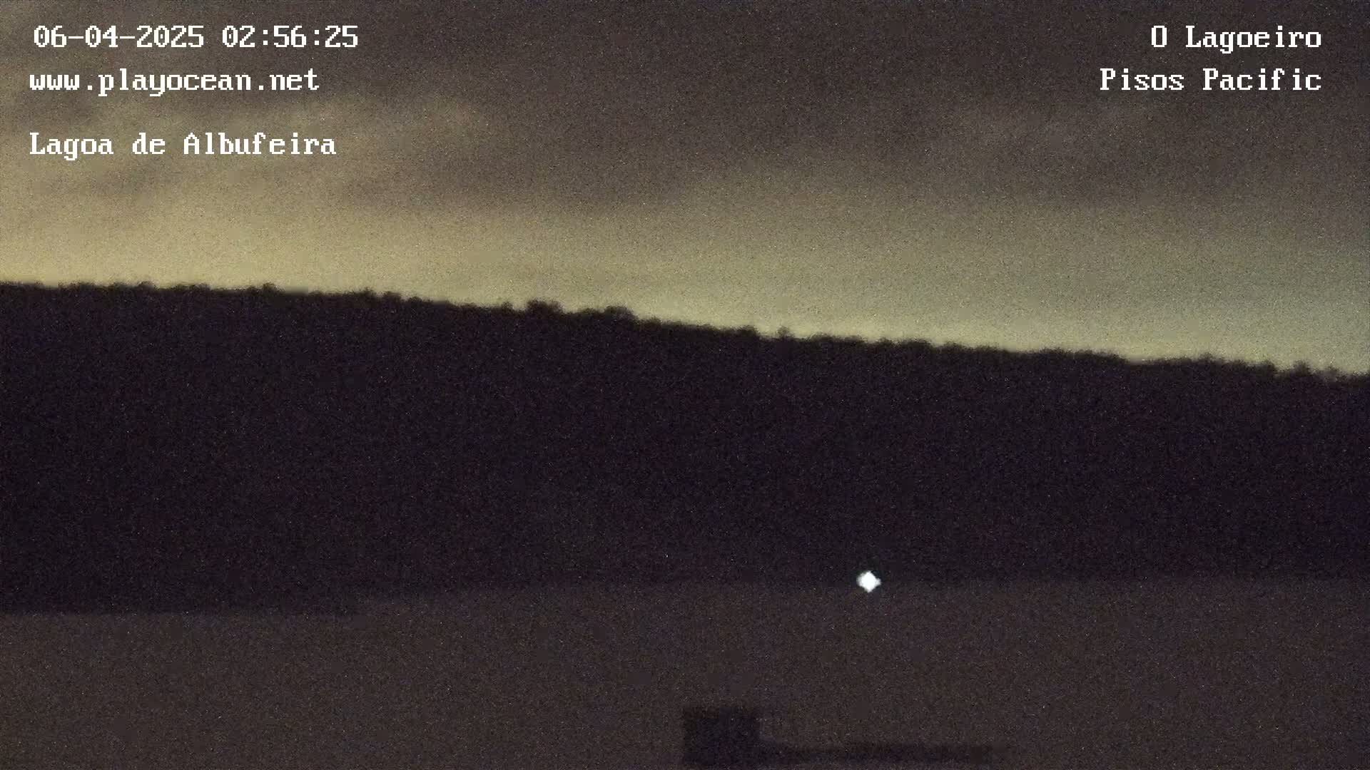 A dark, silhouetted hill line is visible against a pale, dusky sky at night.