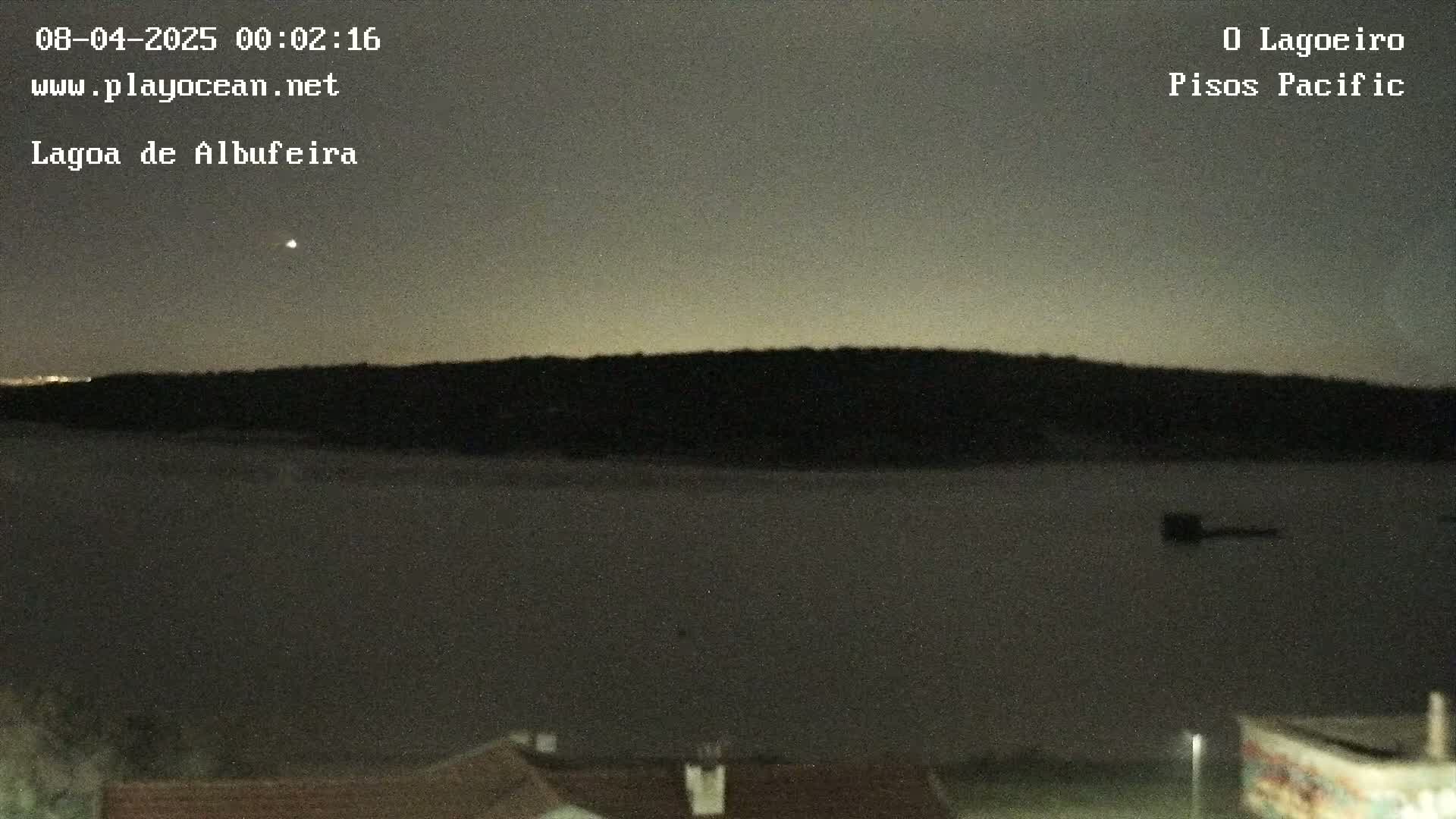 A dark, nighttime view of a body of water with a distant shoreline under a dusky sky.