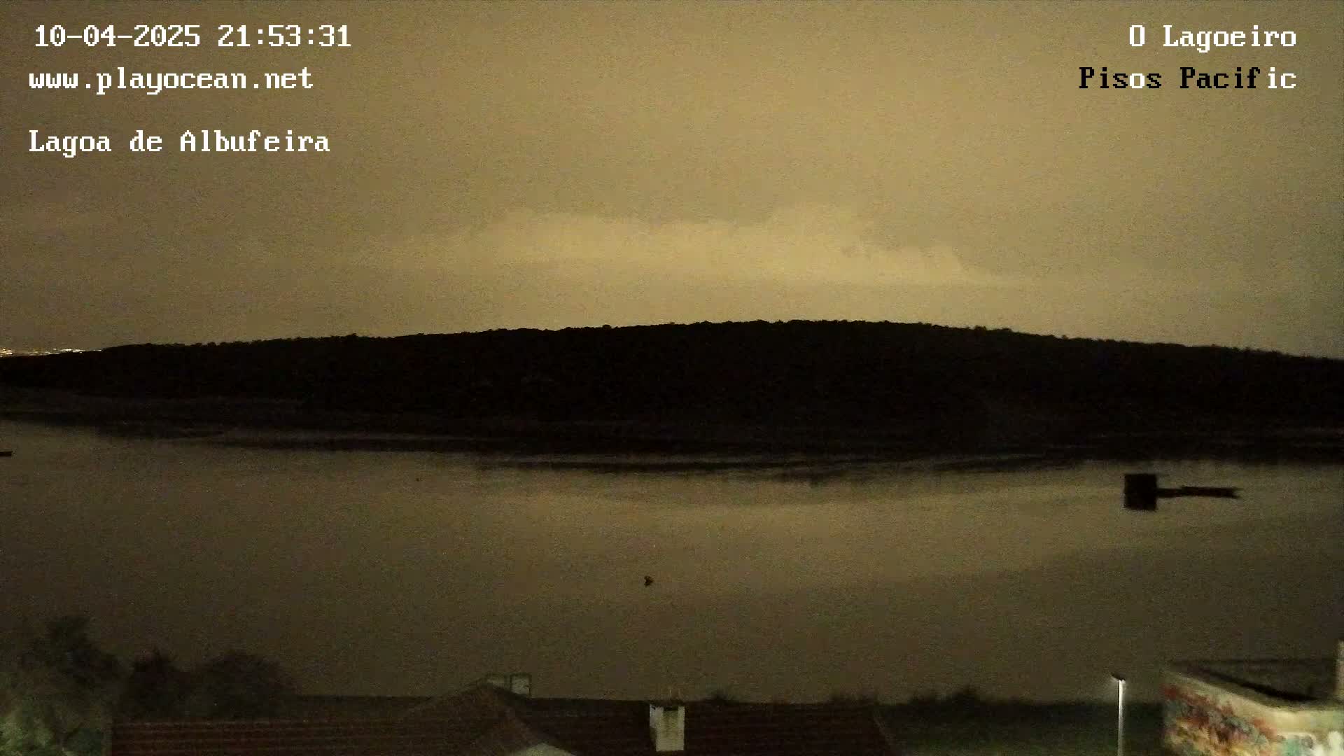 A dark, silhouetted hill is reflected in a calm, brown body of water under a muted, cloudy night sky.