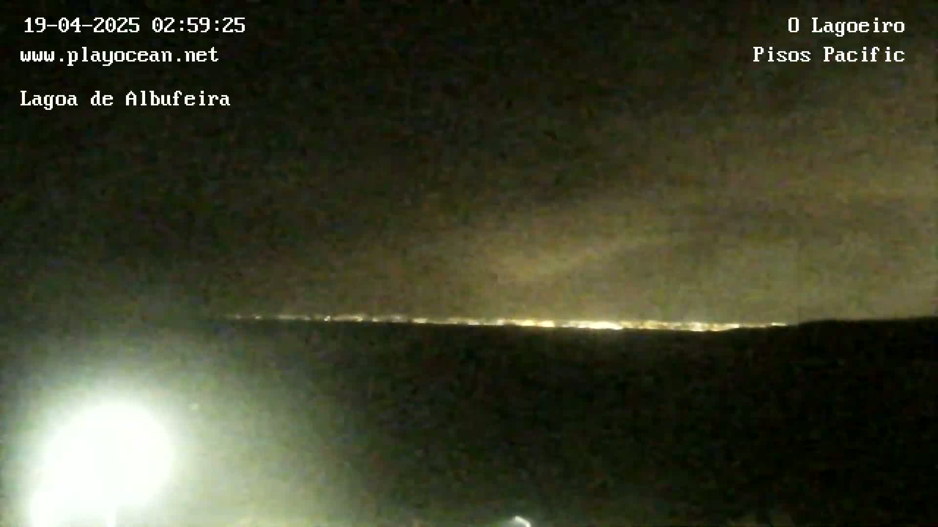 A nighttime view shows a distant line of city lights under a cloudy sky.