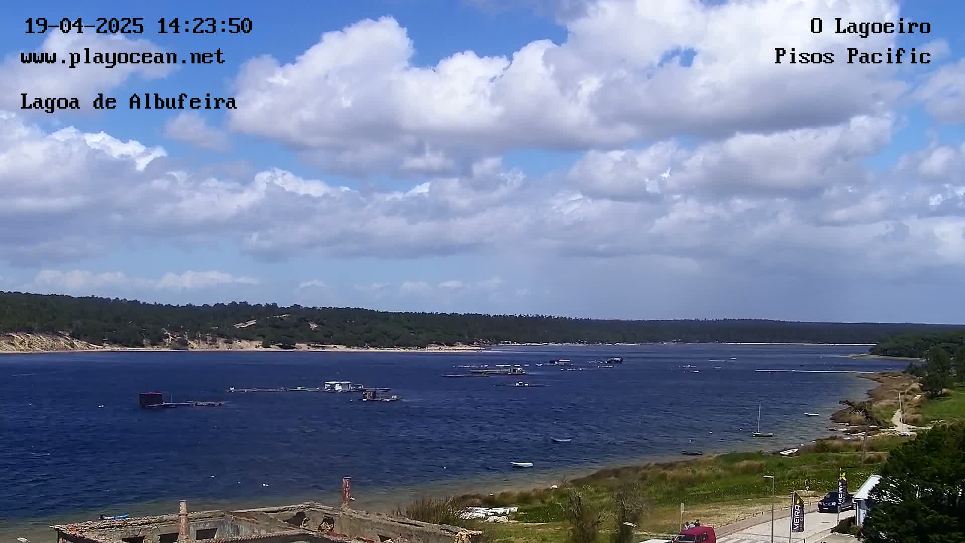 A partly cloudy day overlooks a calm body of water with several structures in the water and a shoreline with green vegetation.