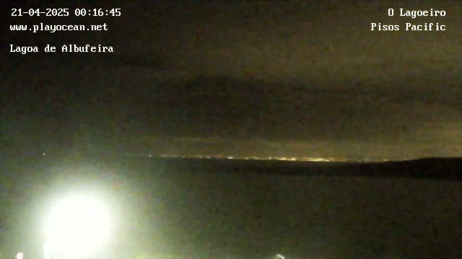 A nighttime long shot shows a dark landscape with a distant line of lights under a cloudy sky.
