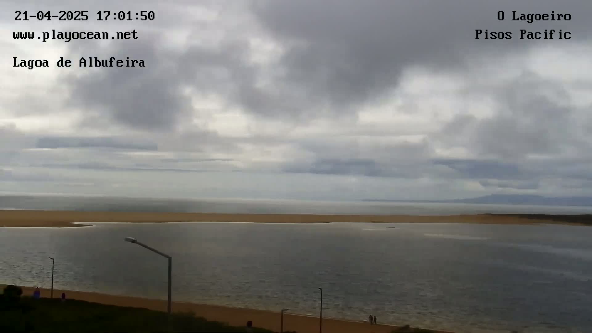 A calm body of water, partially enclosed by a sandy strip of land, stretches out under an overcast sky.