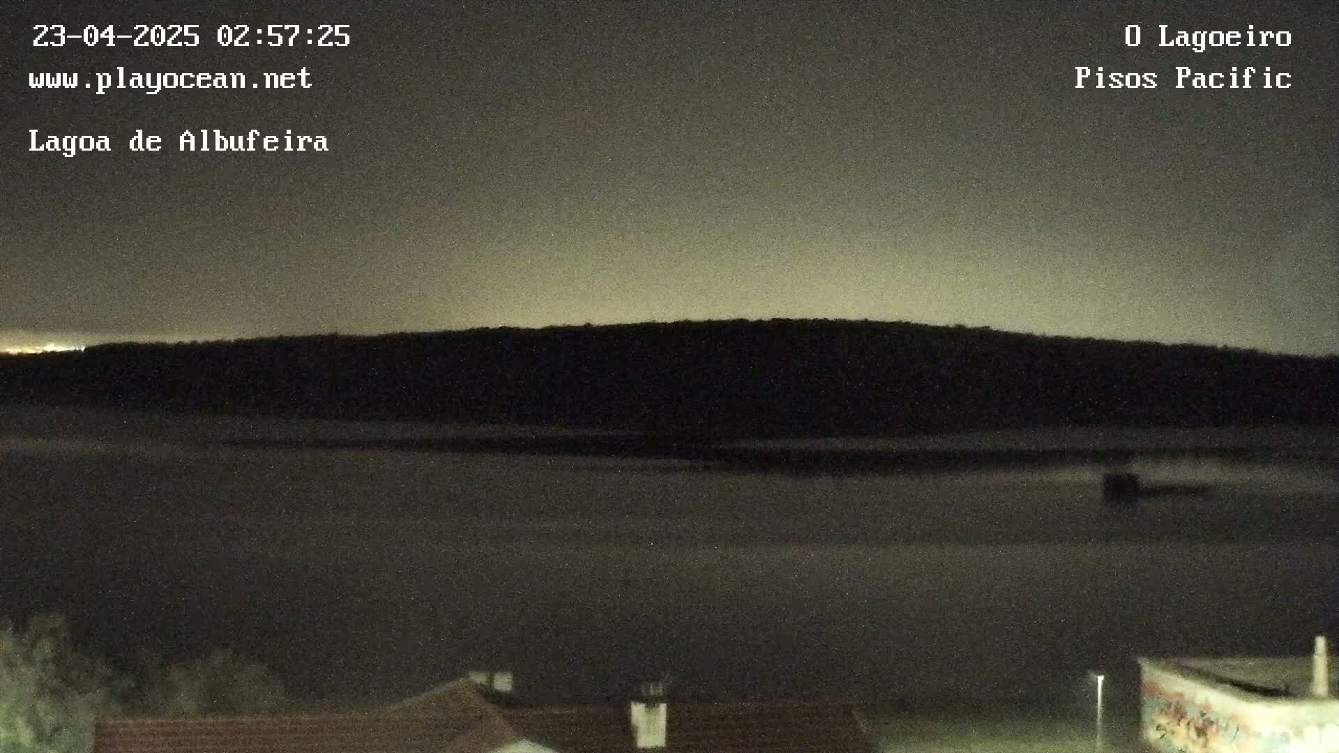 A dark, nighttime view shows a body of water in front of a silhouetted hill under a dusky sky.