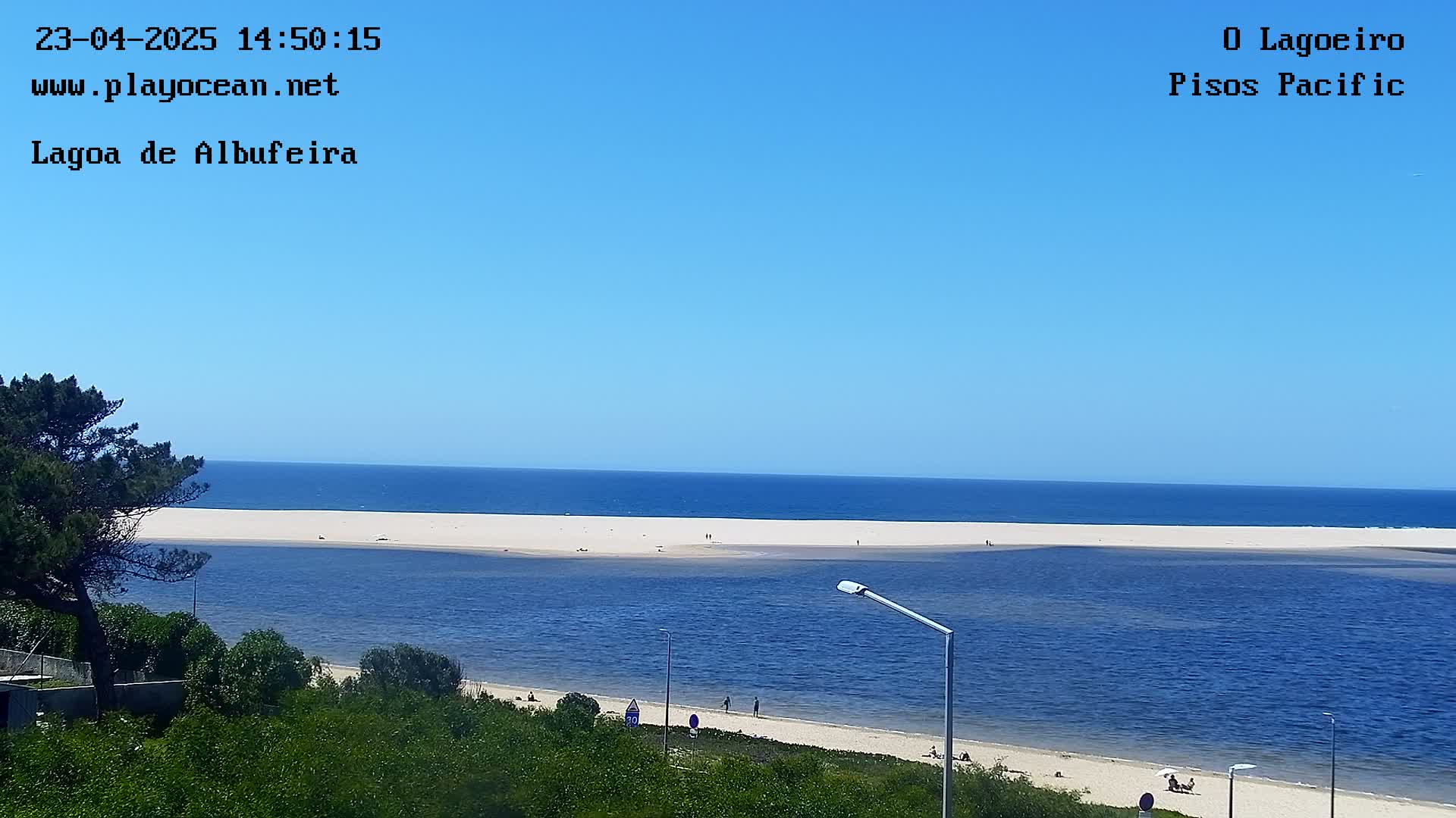 A sandy beach and calm blue ocean are visible under a clear blue sky, with a lagoon separating the beach from a strip of land.