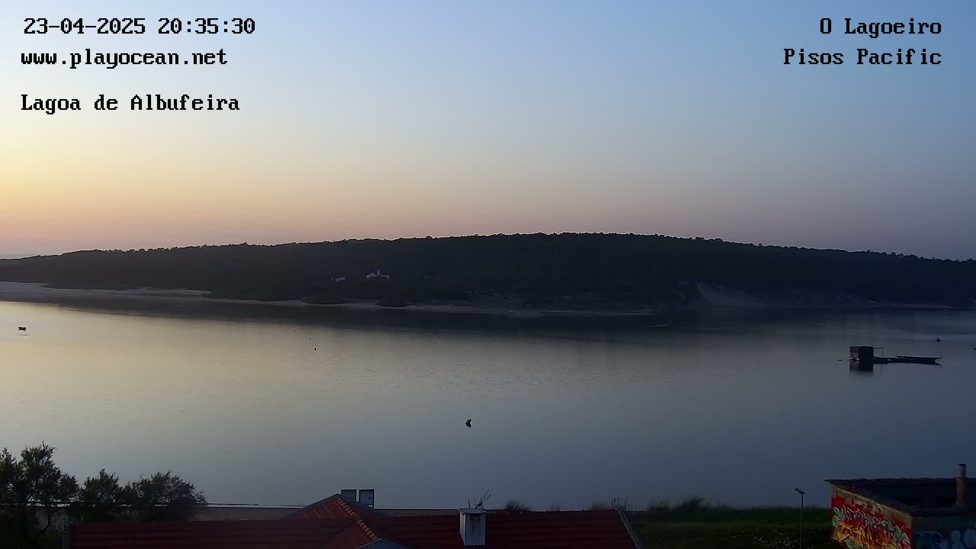 A calm, twilight-lit body of water is seen reflecting the dusky sky, with a dark, tree-covered landmass in the background.