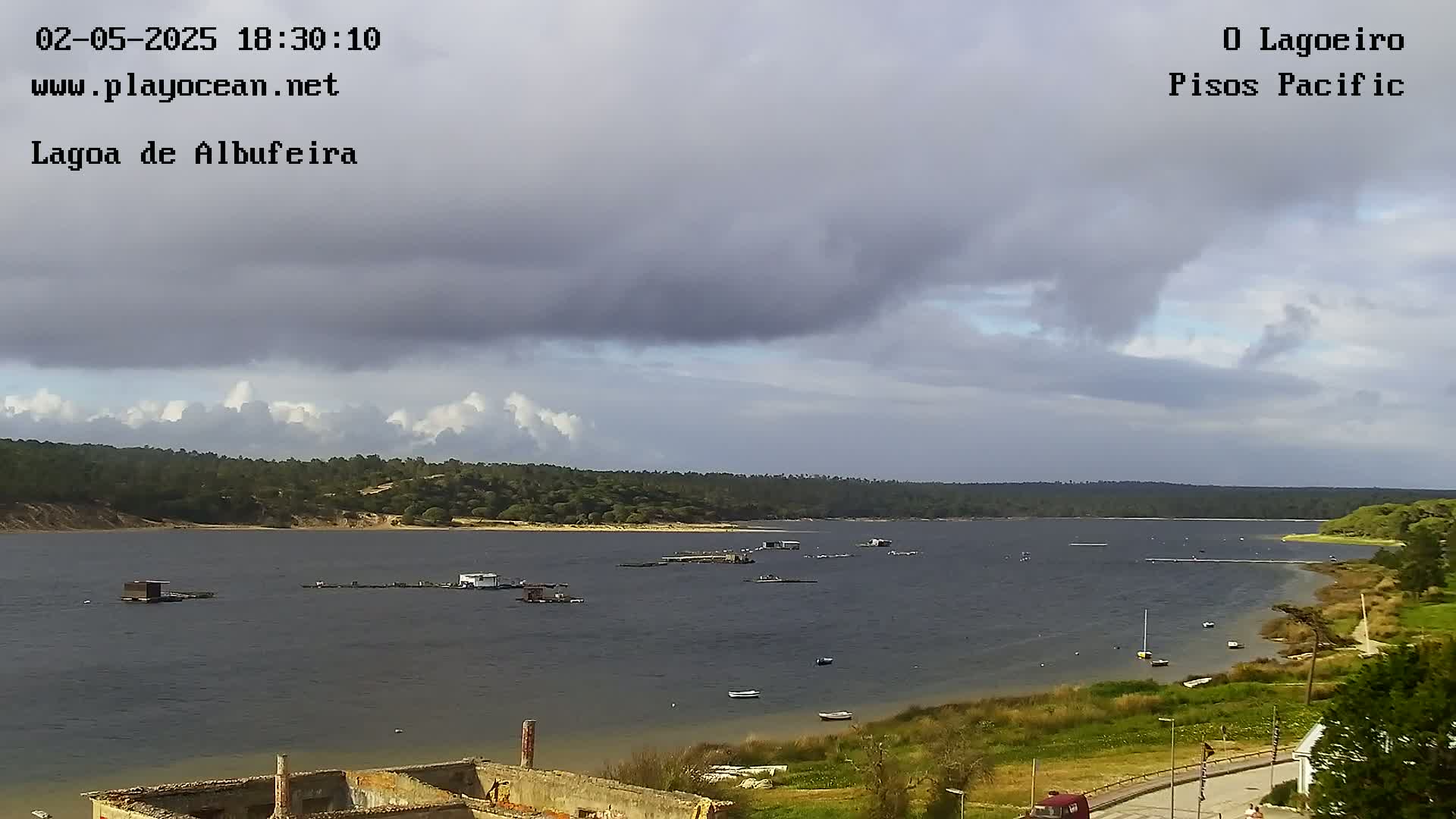 A calm body of water with several small structures and boats is seen under a mostly cloudy sky.