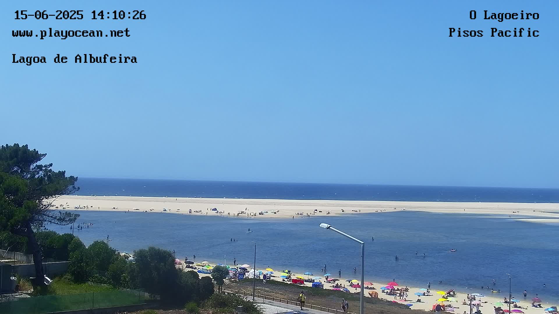A sunny, clear day overlooks a lagoon with many people swimming and relaxing on the beach, and a sandy shoreline leading to the ocean in the distance.