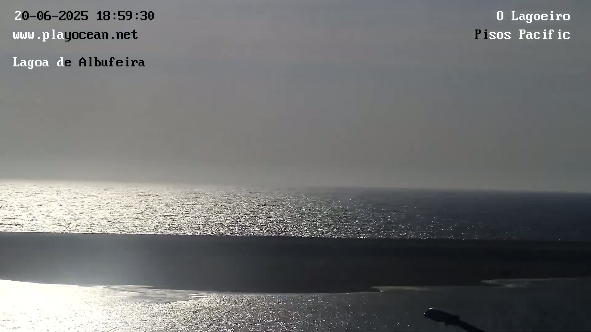 A mostly cloudy sky overlooks a calm, glistening ocean meeting a dark shoreline.