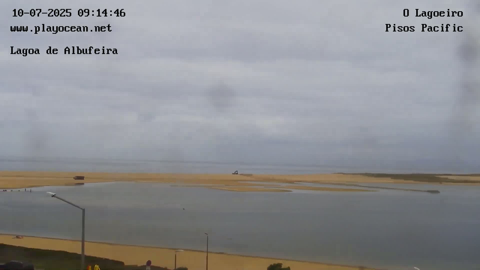 A calm body of water with a sandy shore is visible under an overcast sky.