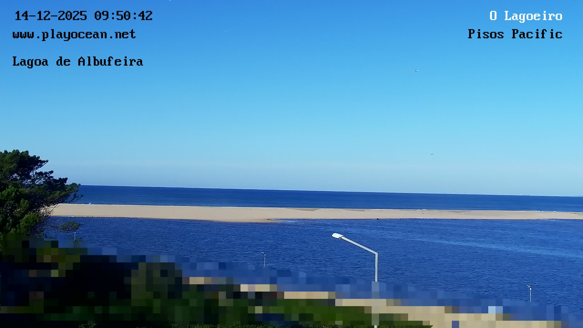 At night, a bright foreground light illuminates a blurry view of a distant city skyline across a body of water under a partly cloudy sky.