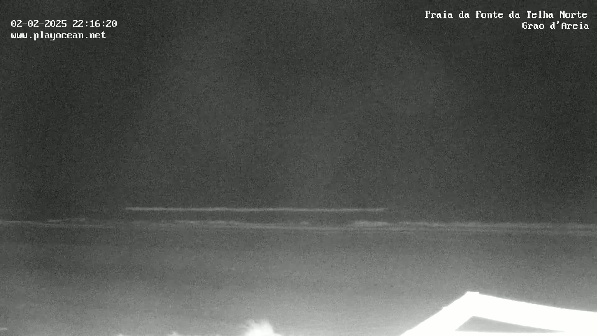A nighttime, low-light view of a dark ocean with a faint line of waves visible near the horizon.