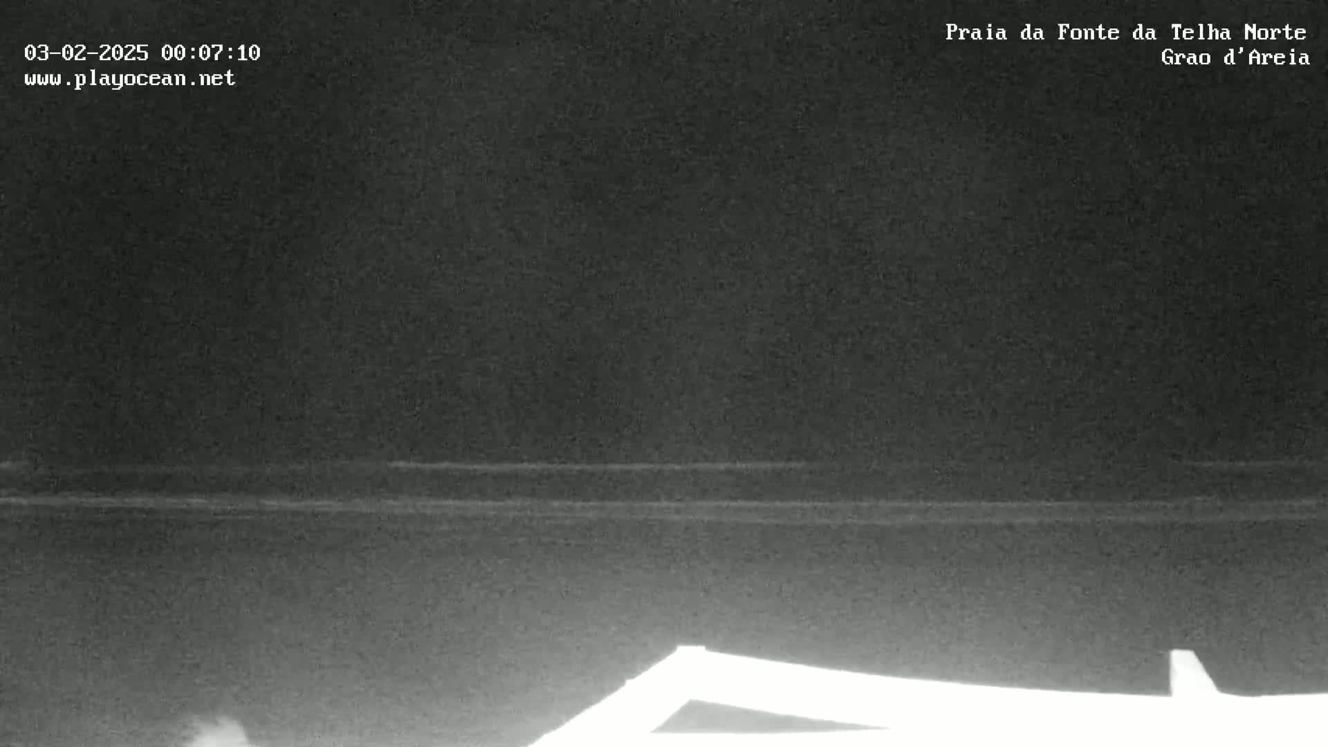 A dark nighttime view of a calm ocean, with a portion of a structure visible in the lower foreground.