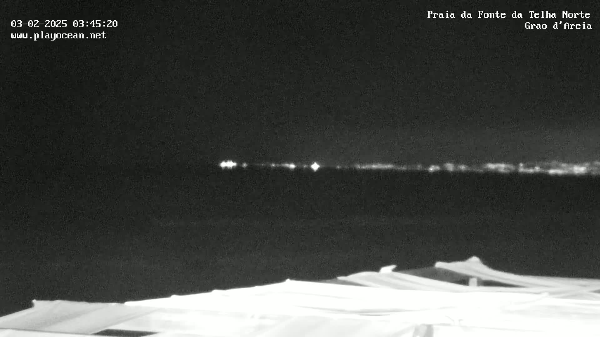 A nighttime view of a dark body of water with a distant, faintly lit shoreline under a clear, dark sky, partially obscured by white objects in the foreground.