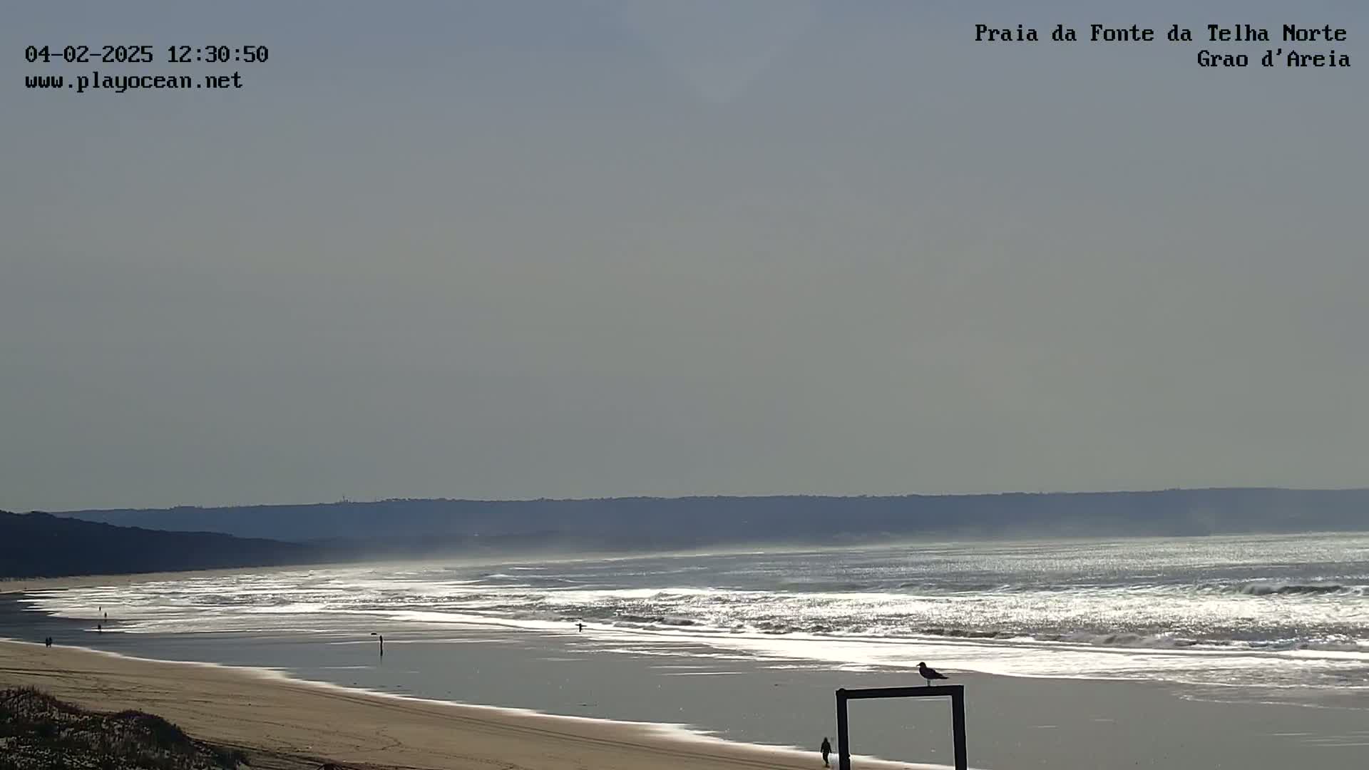 A sandy beach with gentle waves rolls onto the shore under a hazy sky.