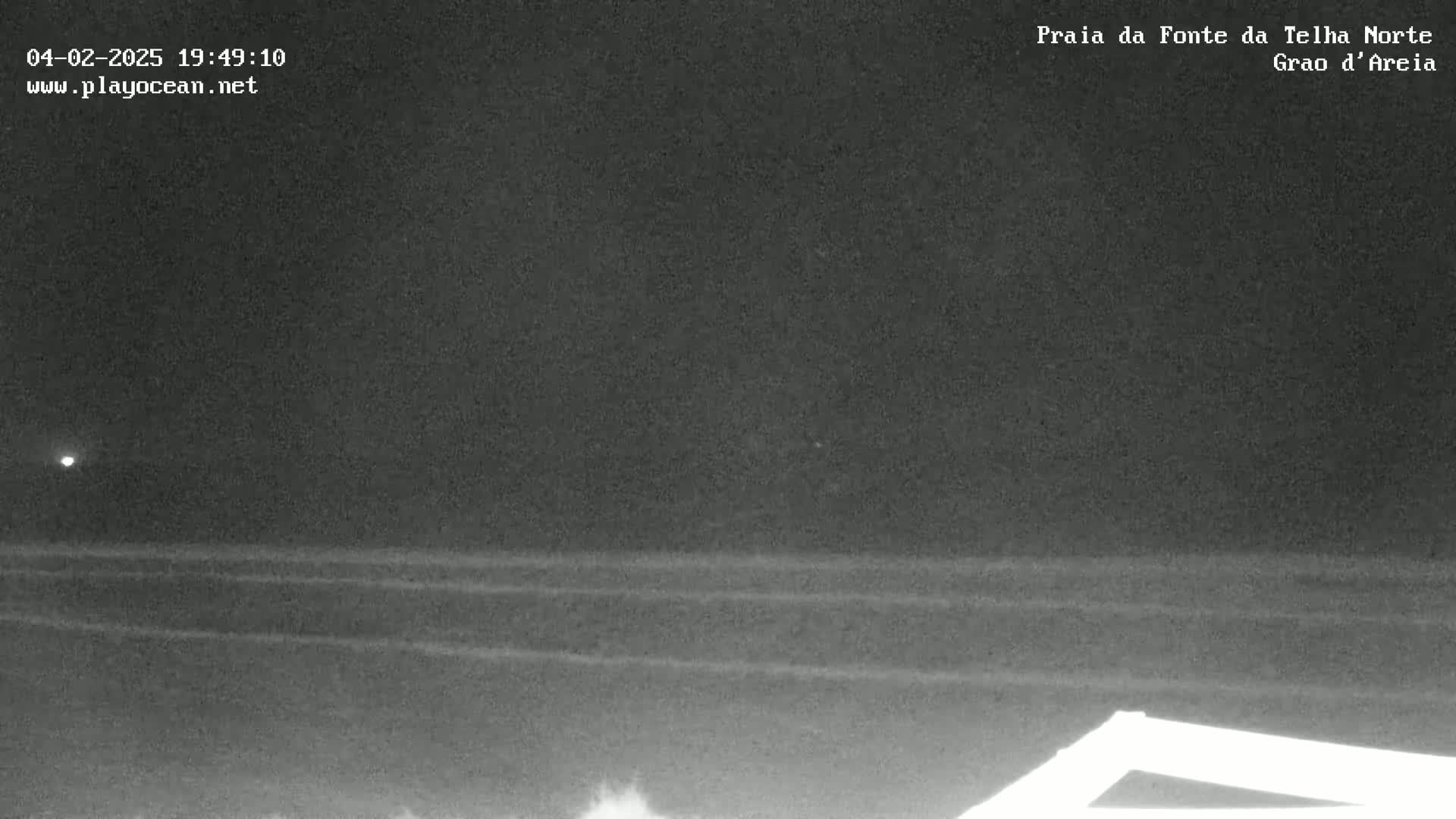A nighttime view of a dark ocean with faint waves under a clear, dark sky.