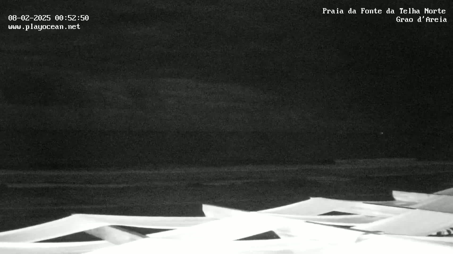 A dark, nighttime beach scene with overcast skies shows numerous beach umbrellas folded and stacked together in the foreground.