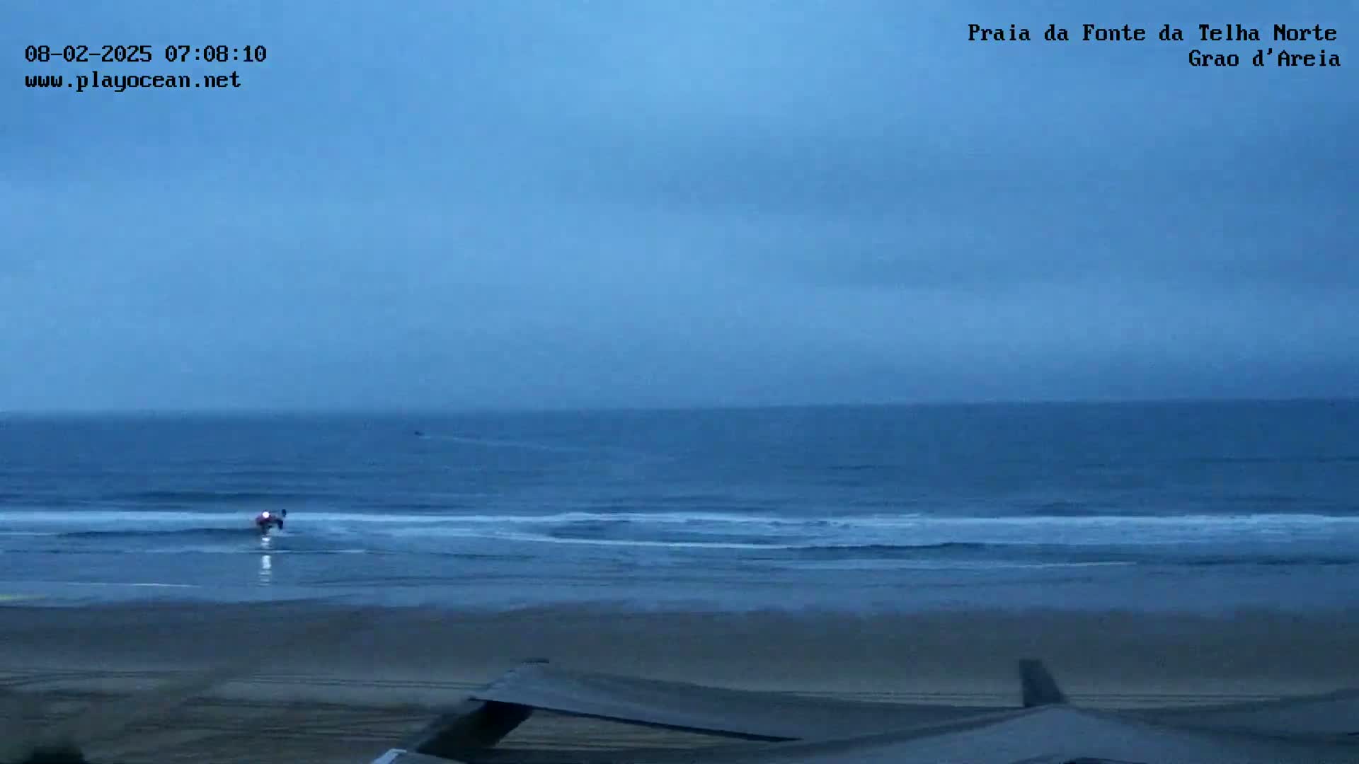 A vehicle is driving on a beach near a dark blue ocean under an overcast sky.
