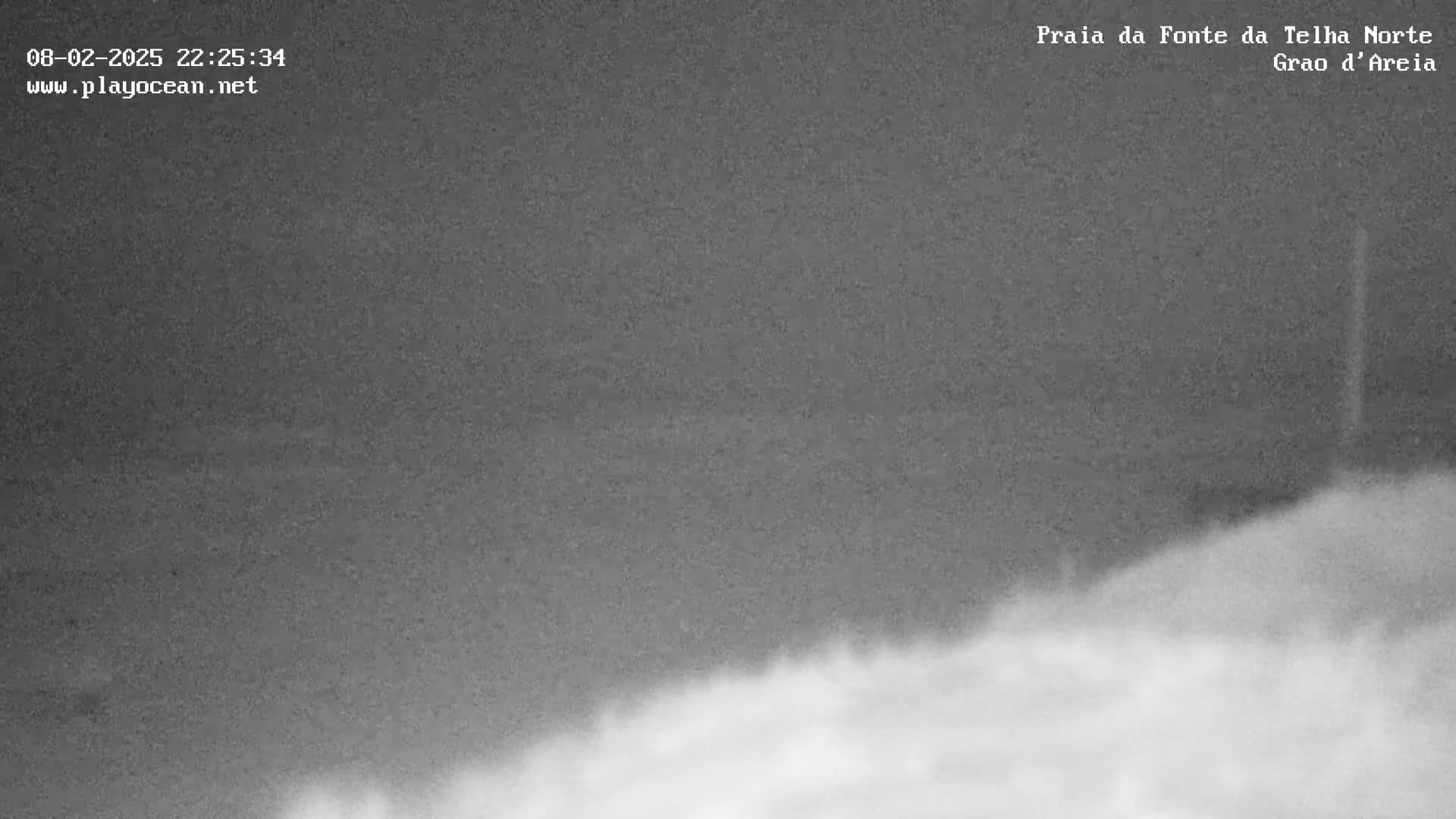 A nighttime, low-light image shows a dark, overcast sky over a dimly lit landscape of sand or beach.