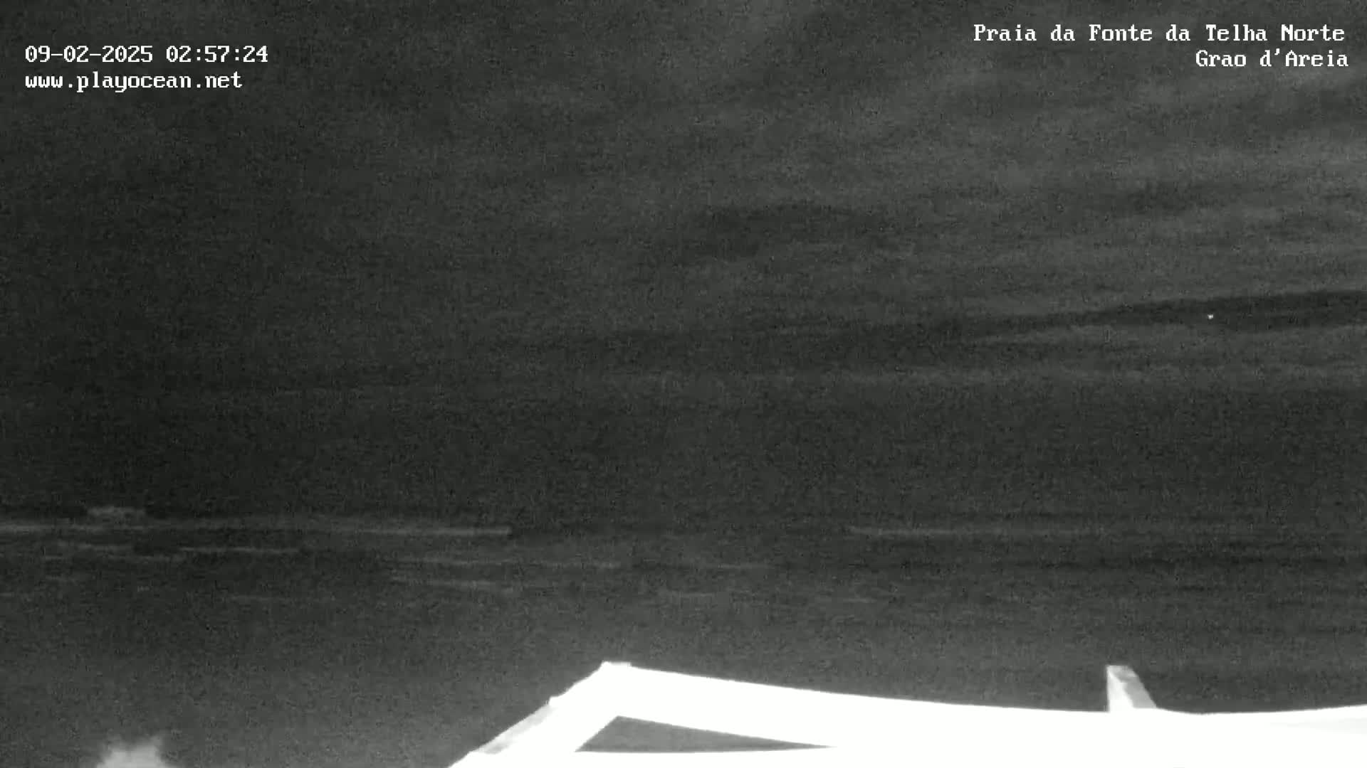 A nighttime, low-light view of a dark ocean with a slightly wavy surface, and a portion of a structure in the bottom right corner.