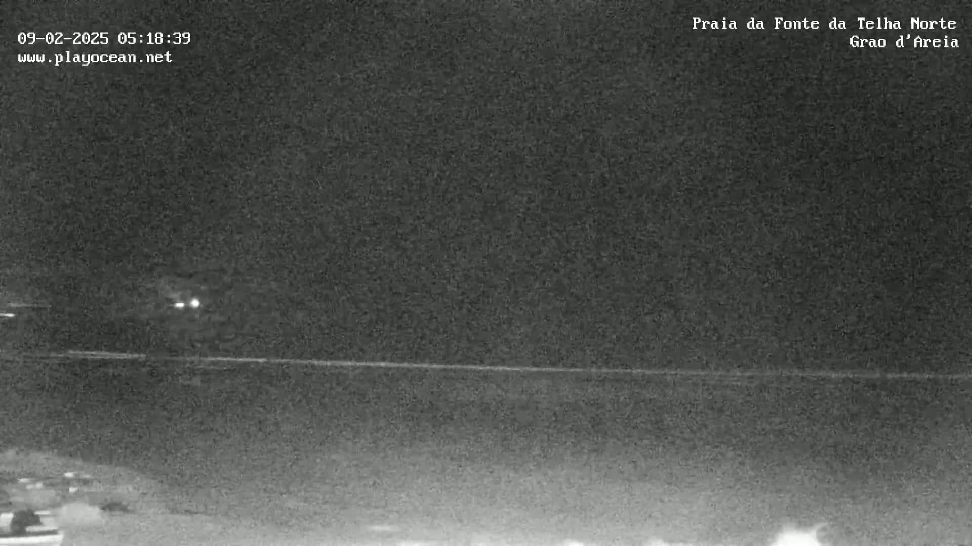 A nighttime, low-light view of a dark beach and ocean under a clear sky.