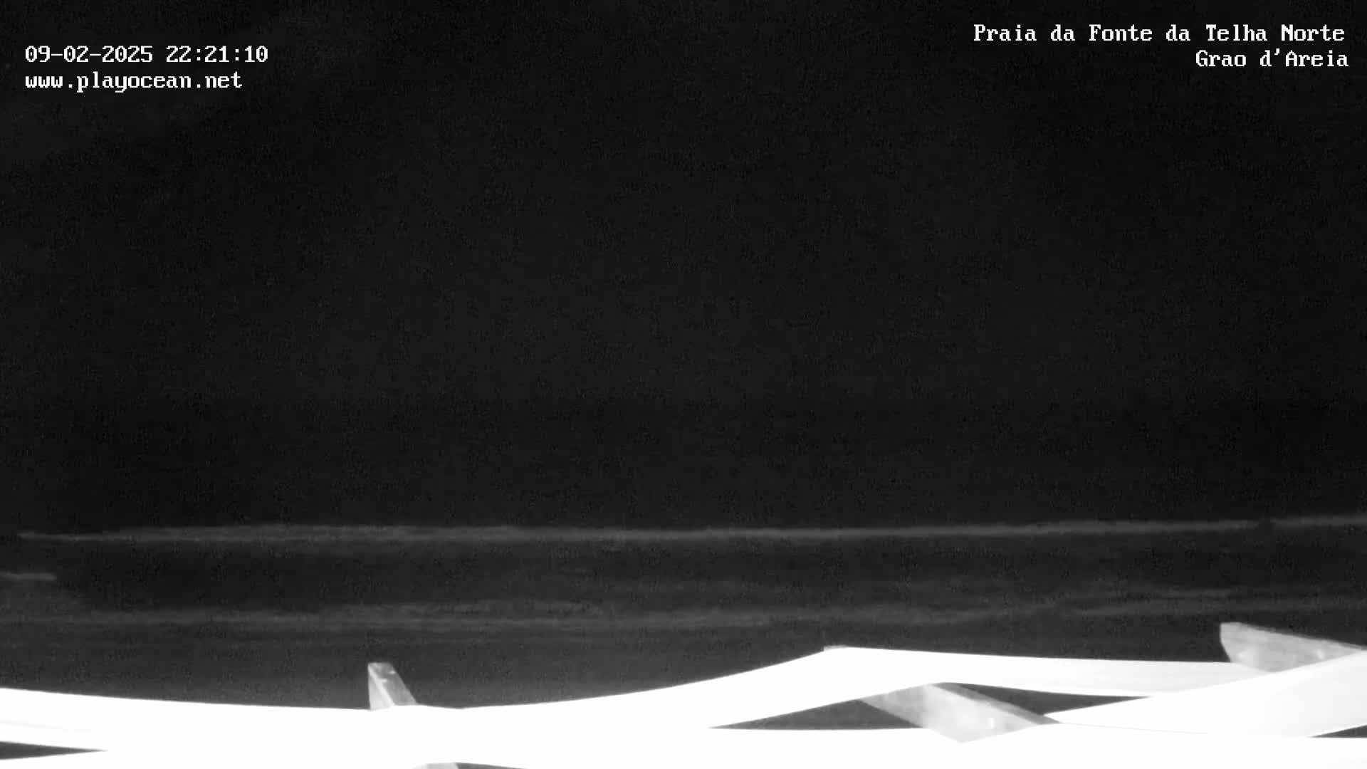 A nighttime, low-light view of a dark beach with gentle waves and a white structure in the foreground.