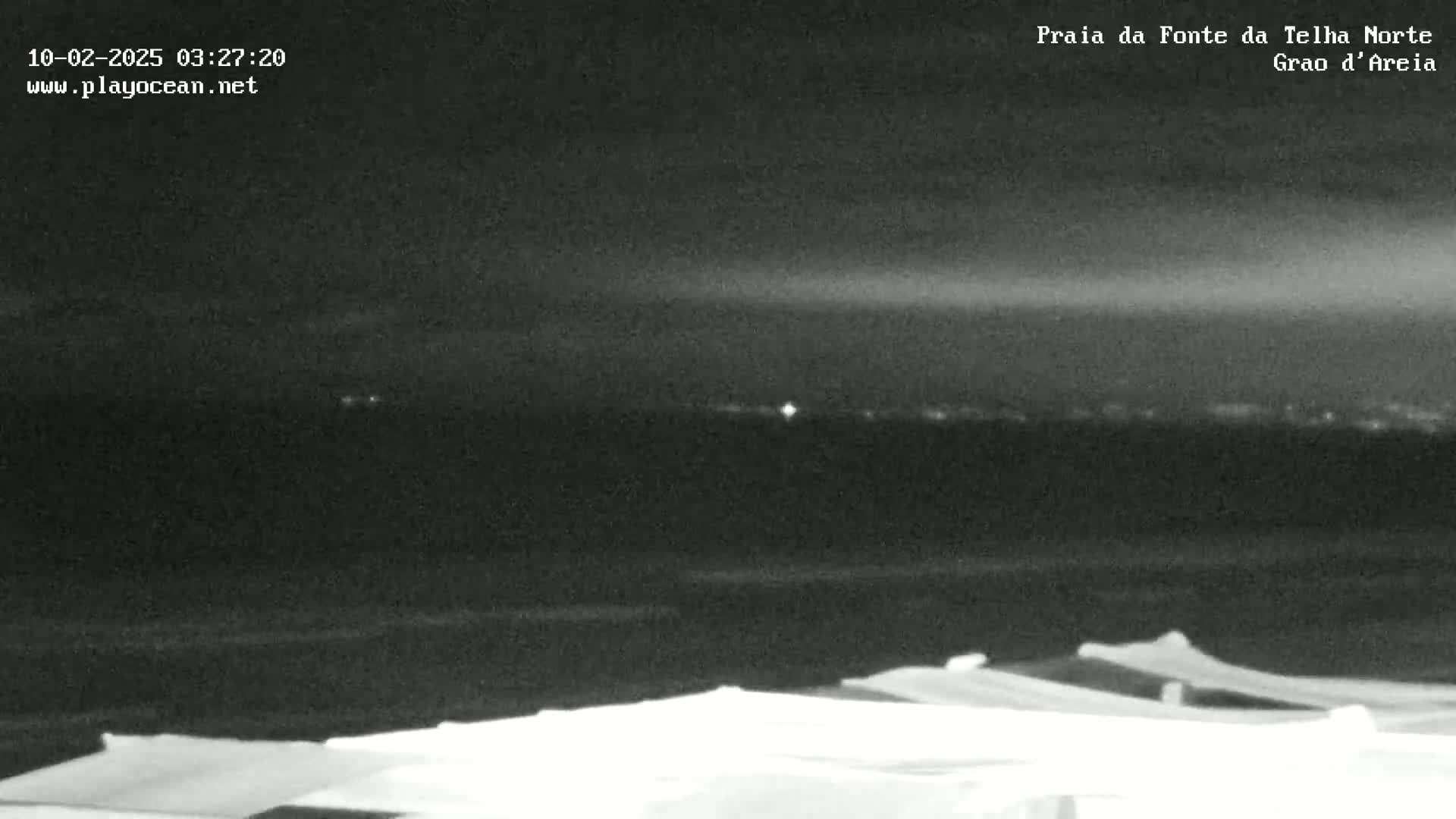 A nighttime, low-light view of a dark beach with several covered objects in the foreground and a dimly lit horizon in the background.