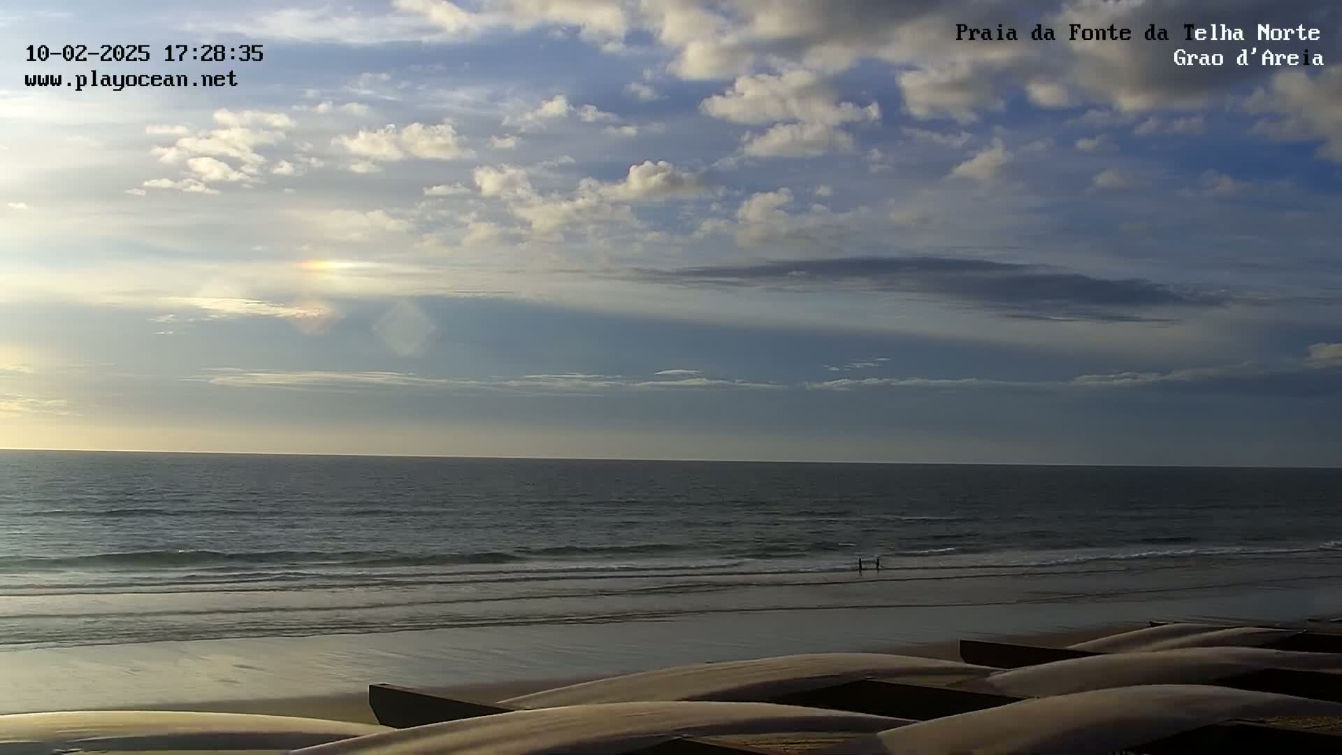 A partly cloudy sky over a calm ocean beach with several boats on the sand.