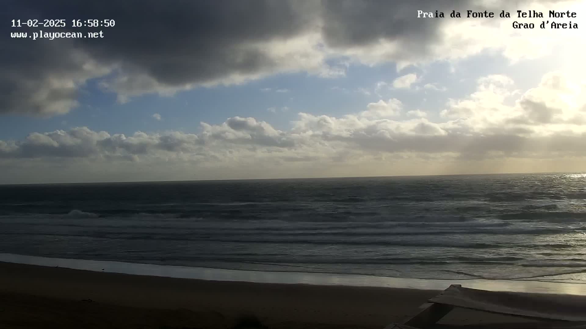 A partly cloudy sky overlooks a dark, wavy ocean meeting a sandy beach.