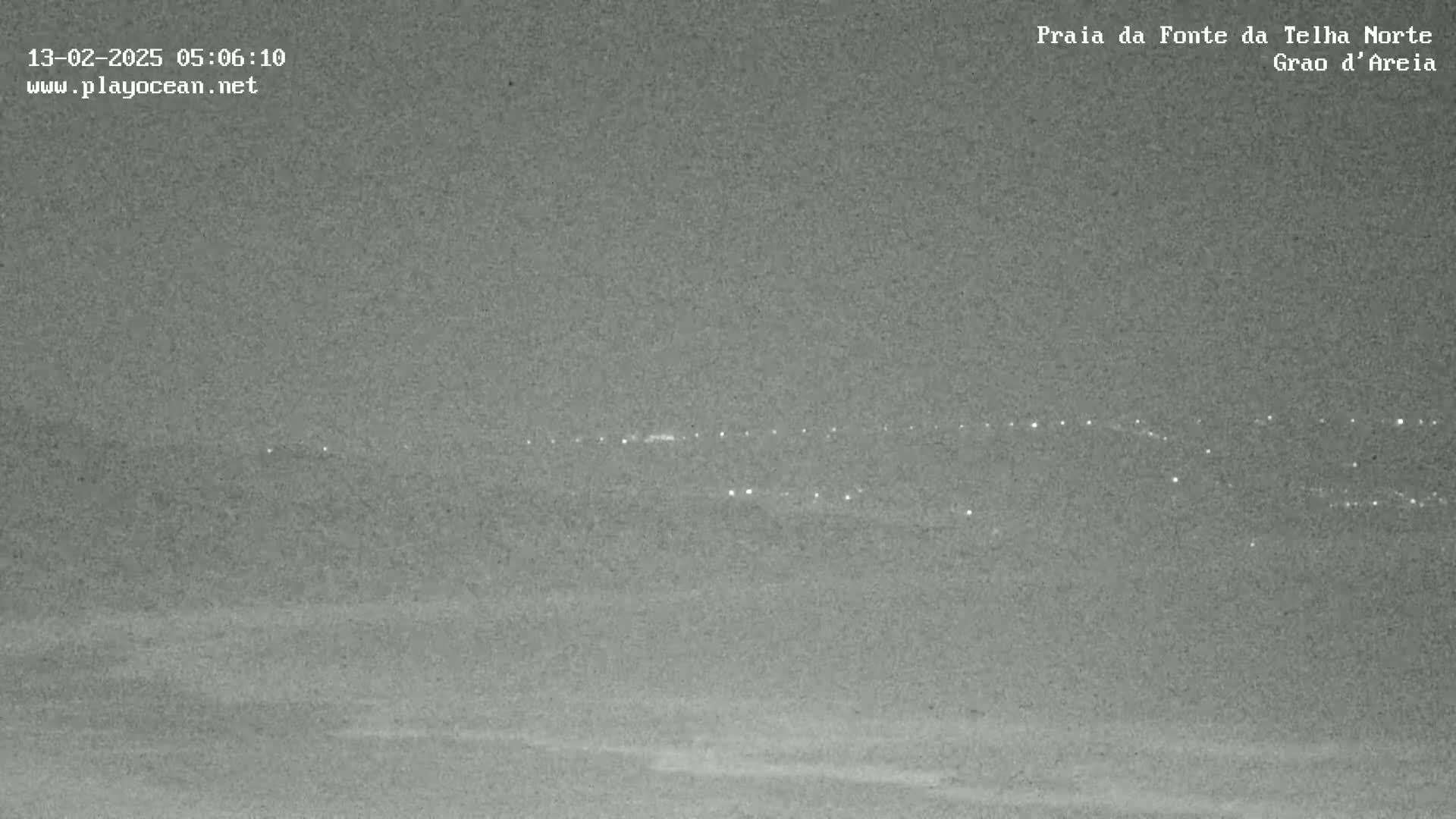 A nighttime, low-light view shows a distant line of lights across a dark, flat landscape.