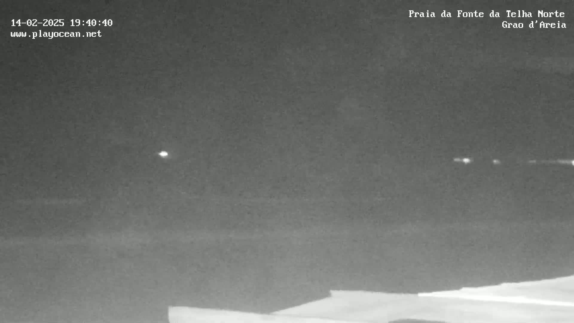 A nighttime, low-light image shows a dark horizon line with several distant, faint lights visible.