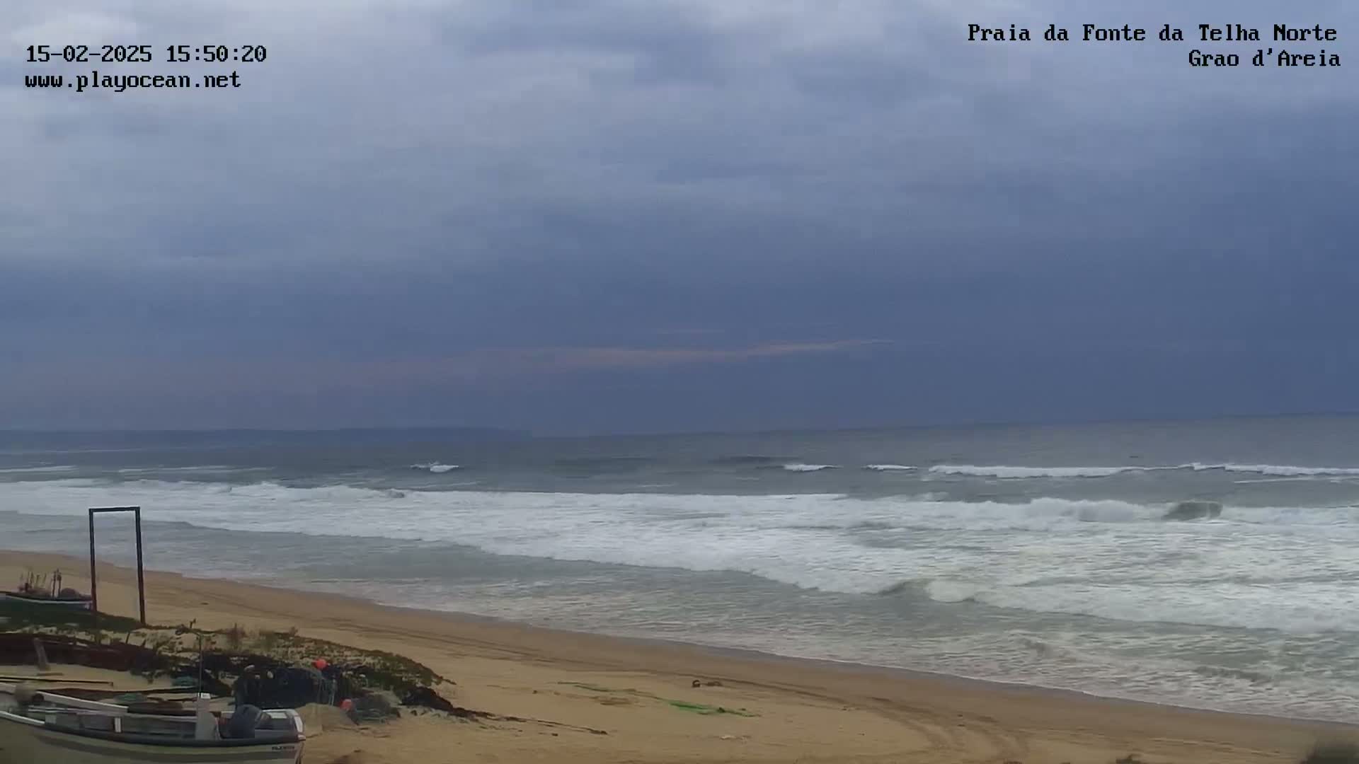 A sandy beach with moderate waves rolls onto the shore under an overcast sky.