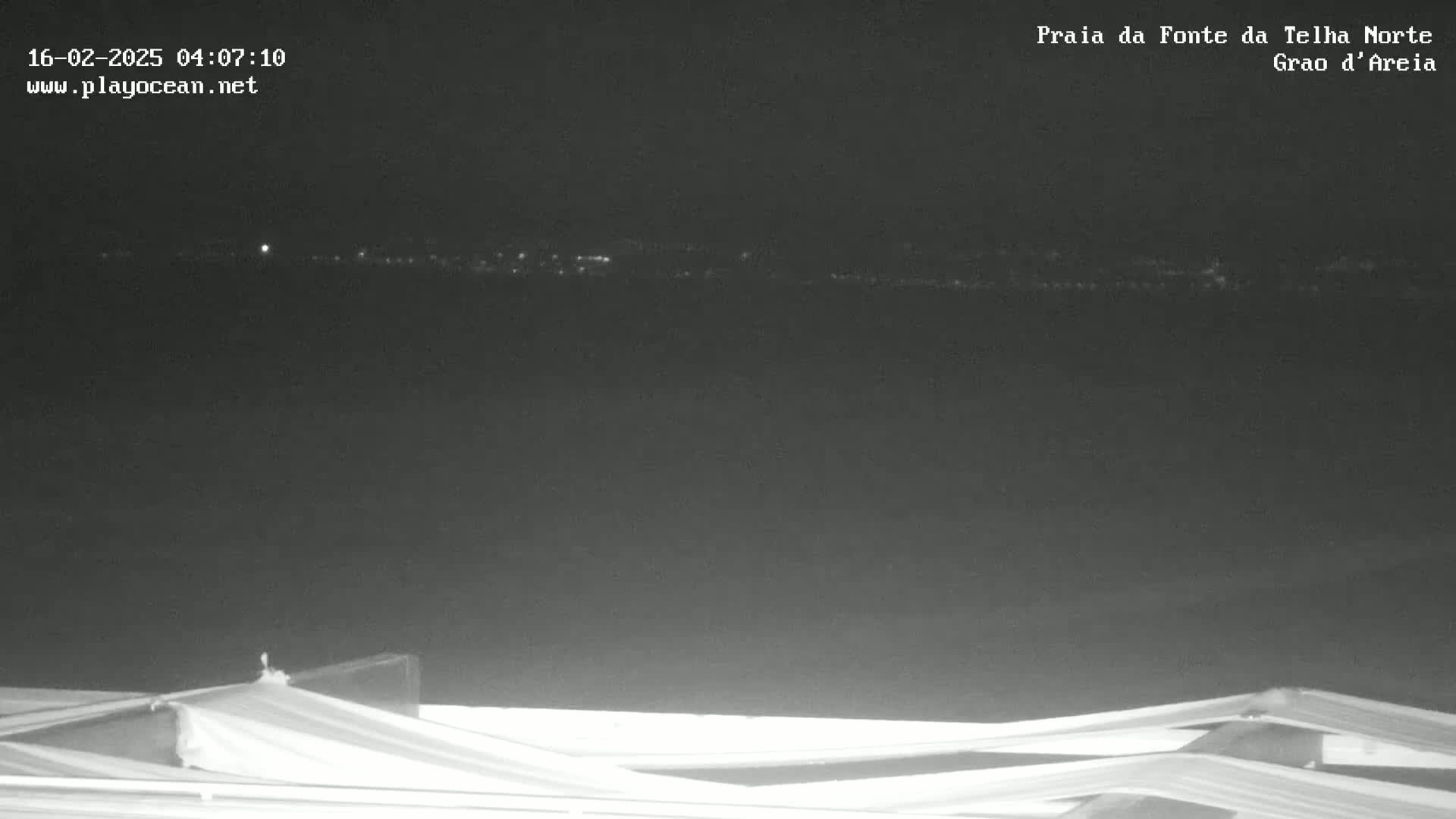A nighttime view of a dark body of water with a faint line of lights on the horizon, partially obscured by a white structure in the foreground.