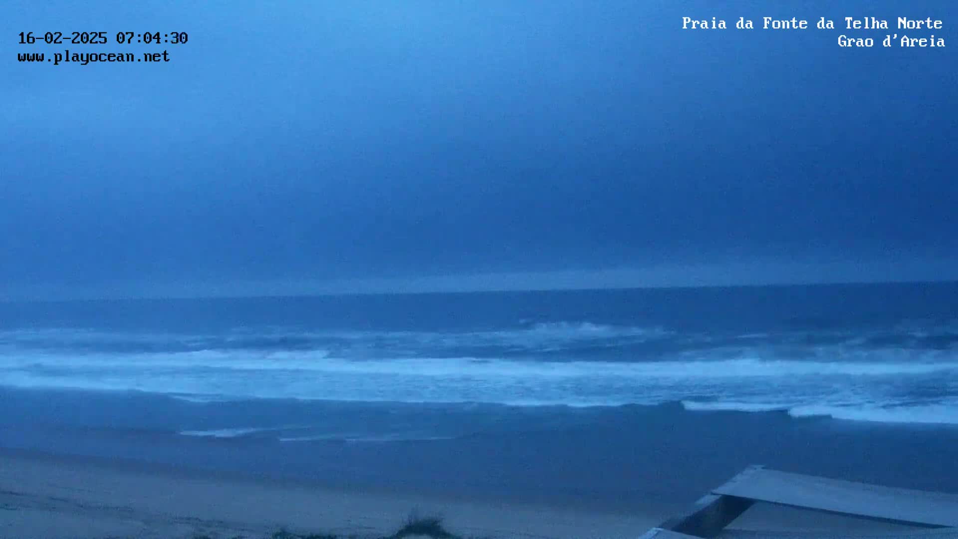 A mostly cloudy, overcast sky hangs over a wavy ocean meeting a sandy beach.