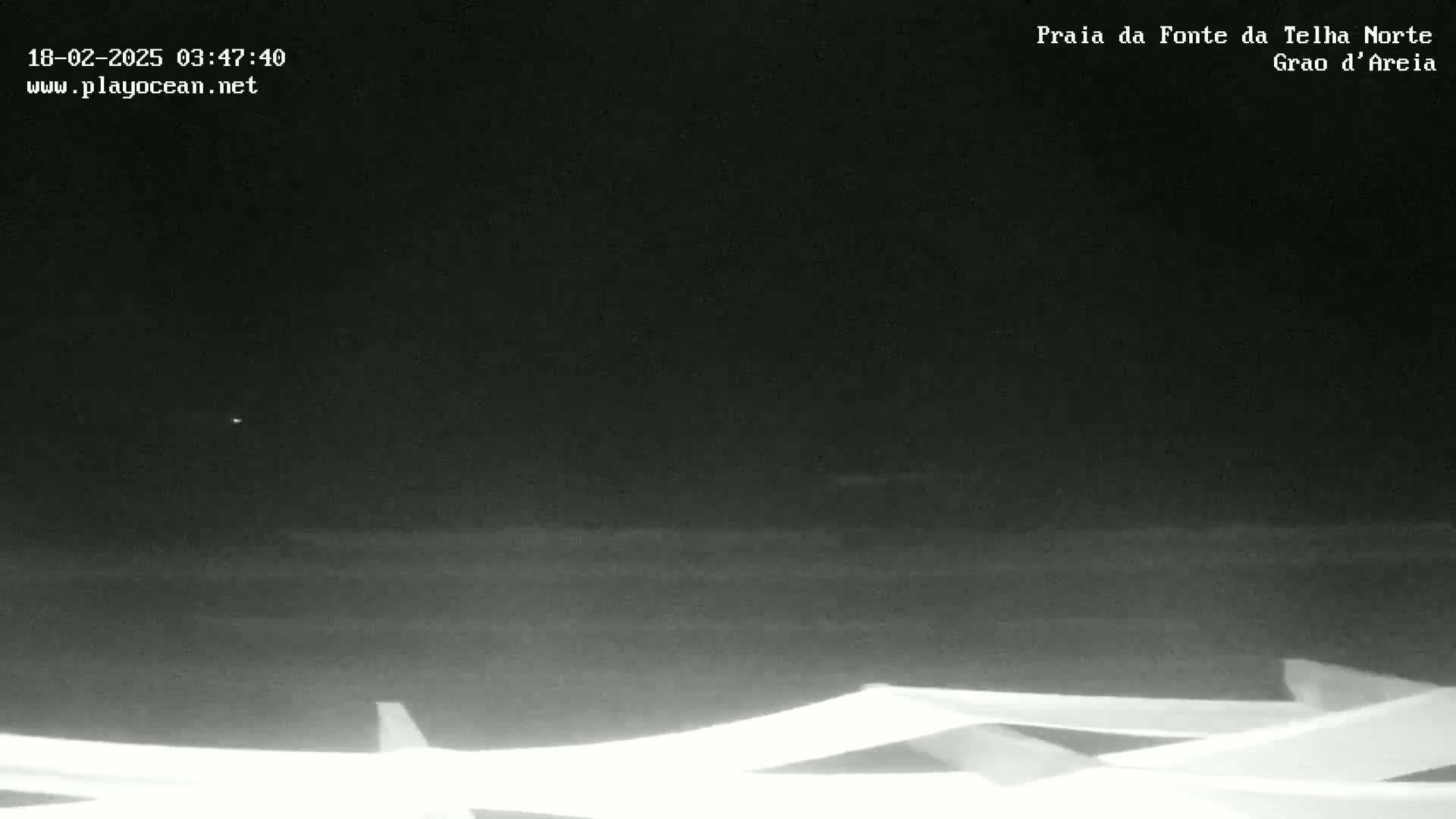 A nighttime, low-light view of a dark ocean with a dark sky, showing the top of a white structure in the foreground.