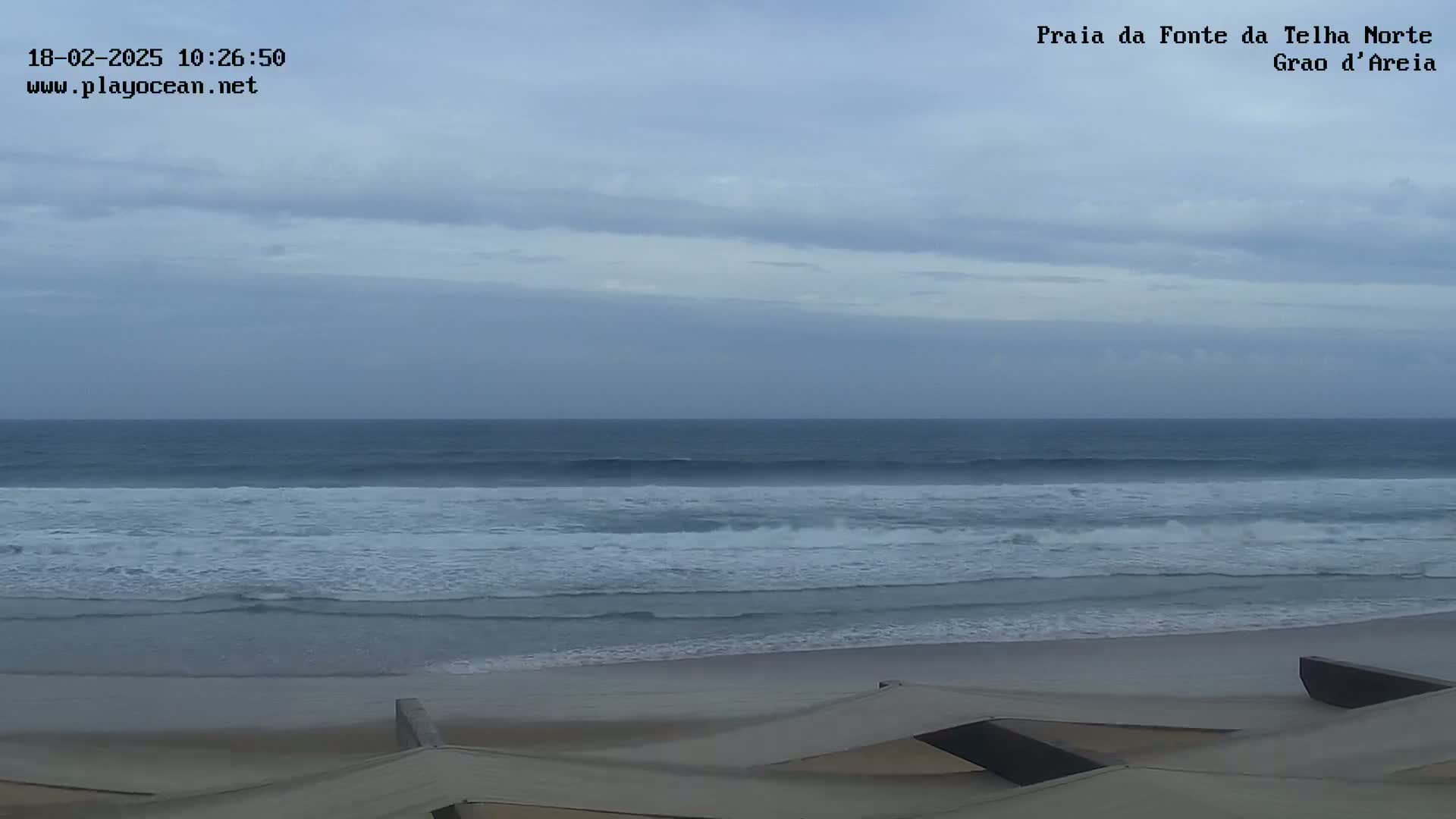 An overcast sky hangs over a beach with moderate waves rolling onto the shore.